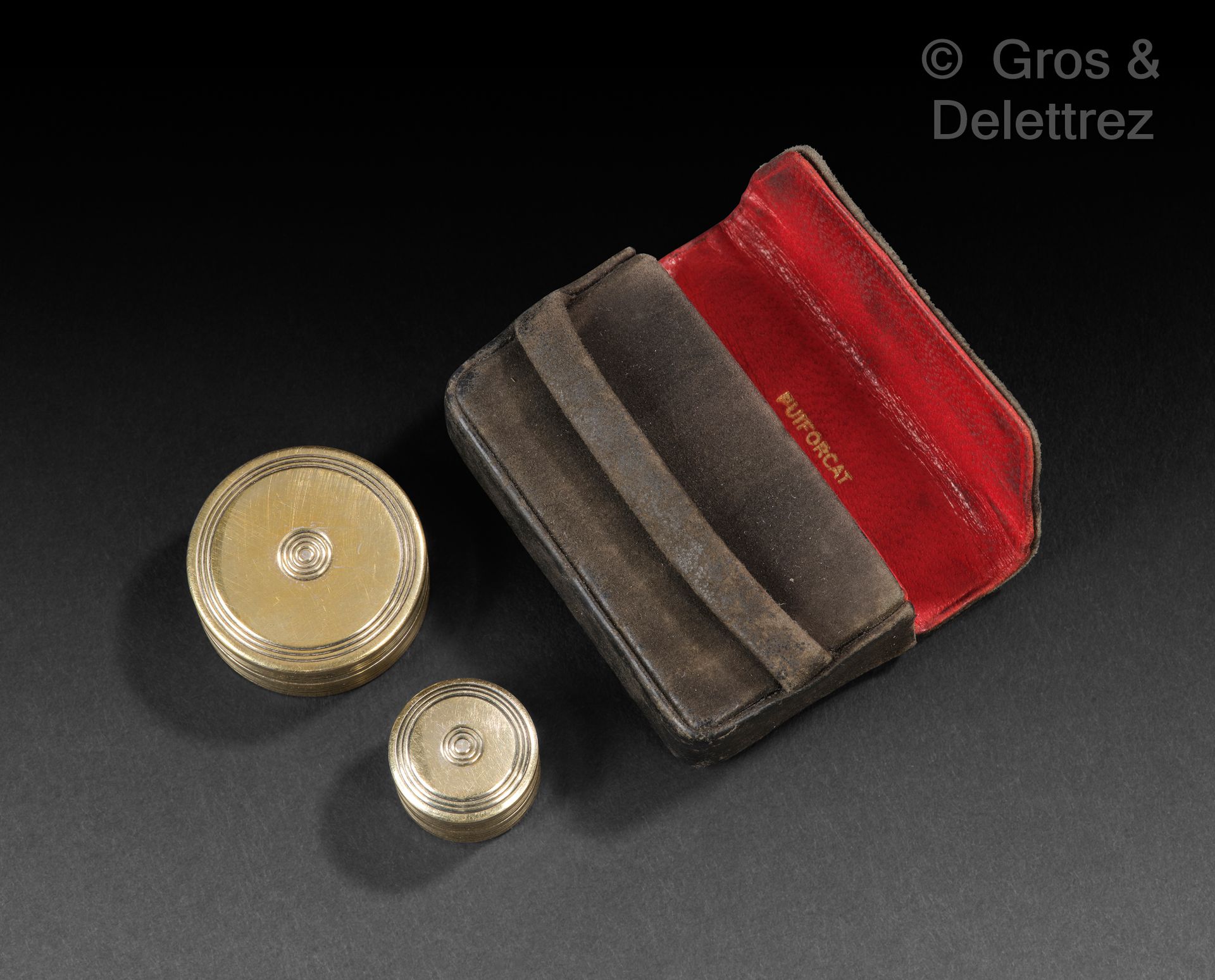 Null PUIFORCAT

两个圆形的微型镀金药盒，上面刻有网状的装饰。



重量：15克。直径：2,6和1,6厘米

装在一个有红色衬里的黑色皮箱里。