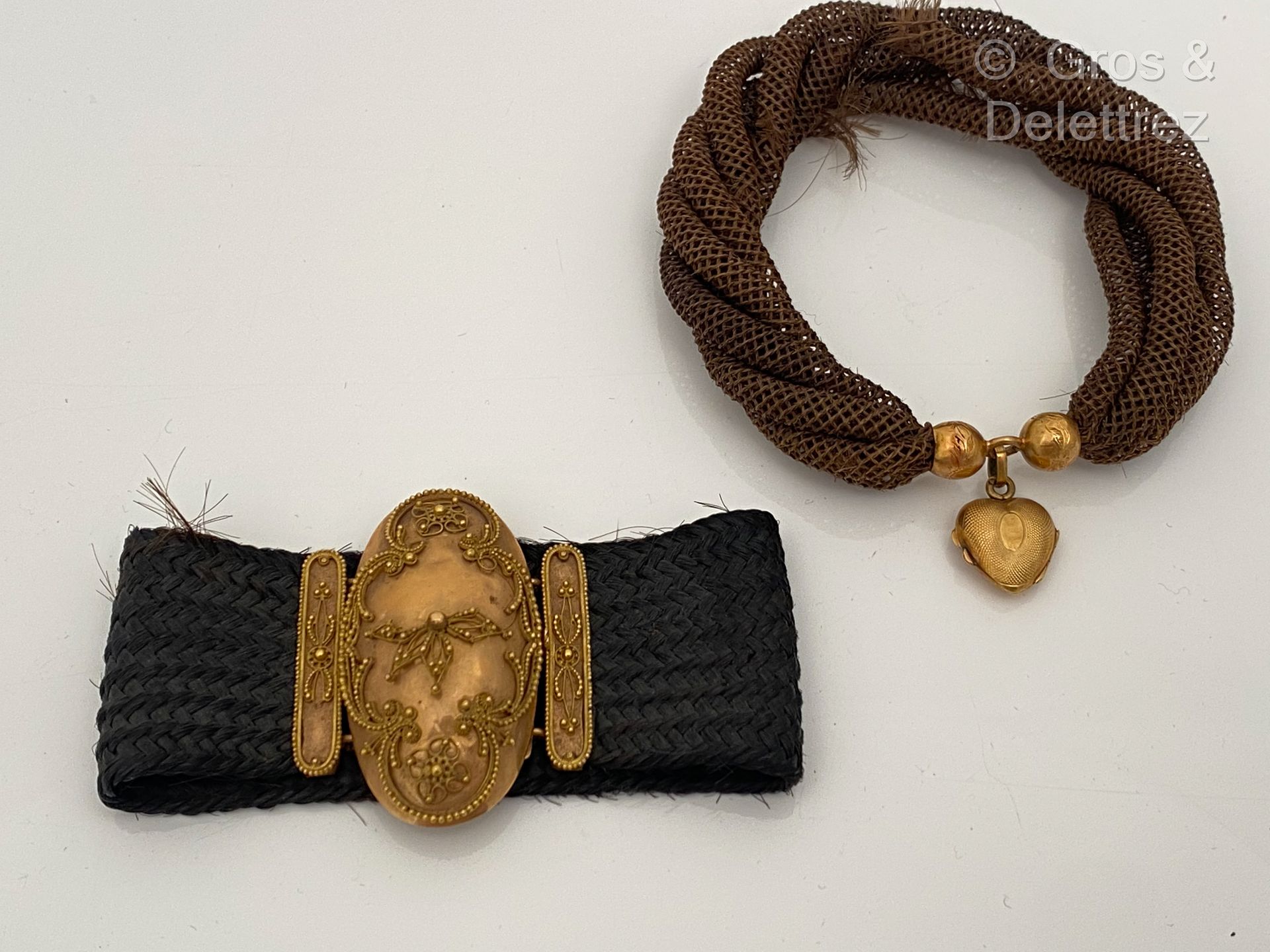 Null 一套两个编发的手镯，其中一个突出了黄金錾刻的珍珠，拿着一个心形的 "Porte-souvenir "吊坠；另一个是椭圆形的扣子，突出了丝线交错的特点（&hellip;