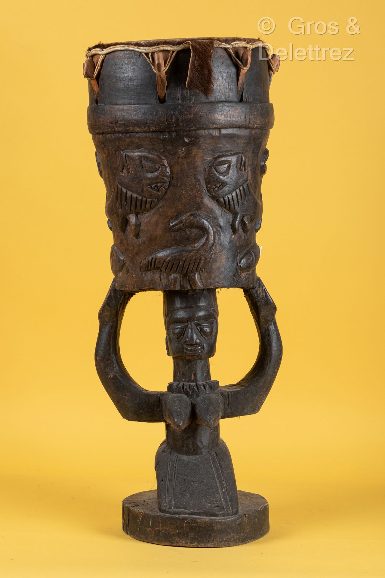 Style Senoufo, COTE D’IVOIRE 一件涂有铜绿的木鼓，雕刻着一个女人抬着头，箱子上有狮子、蛇、鱼、鸟和乌龟的轻浮装饰。
高度：77厘米。