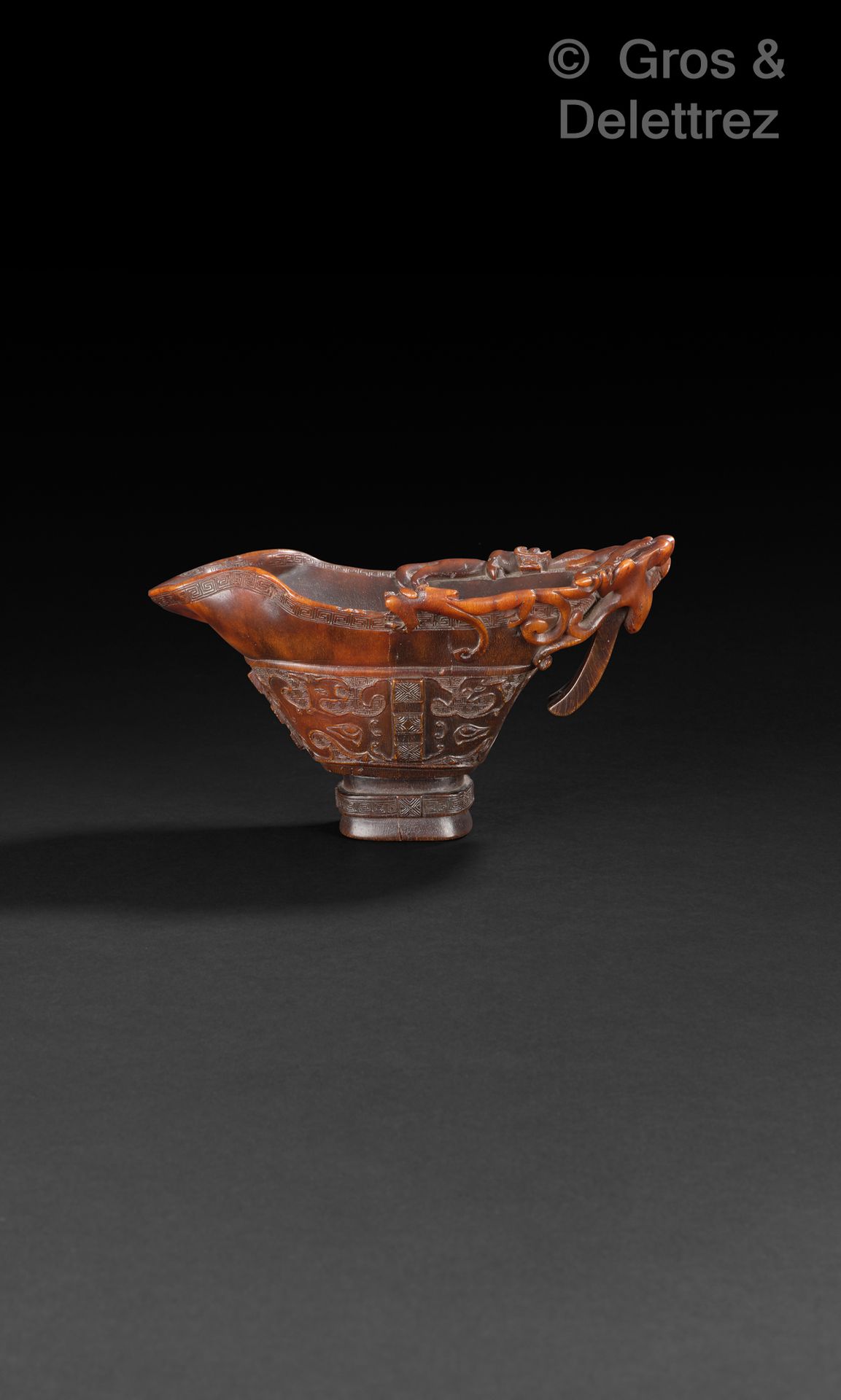 Null 一个重要的犀牛角酒杯，放置在一个装饰有希腊图案的底座上，杯口装饰有包括饕餮面具在内的古代图案。手柄精雕细琢，镂空有四条龙。
中国，18世纪
H.10.&hellip;