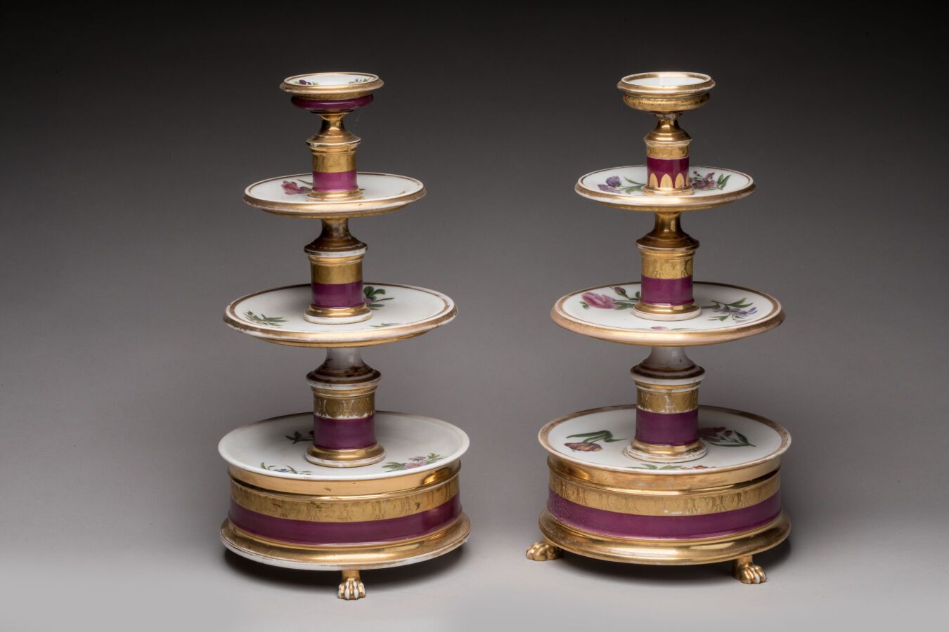 Null 巴黎。一对有四层的瓷质蛋糕架，装饰有紫色丝带和金色花环，部分点缀有玛瑙和多色花。帝国时期。高41厘米，长23厘米。磨损的黄金，一个有污点。