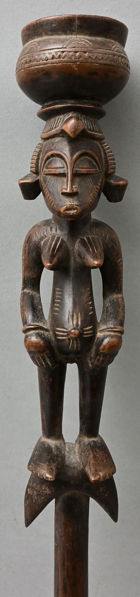 Null 礼仪杖，塞努弗风格（象牙海岸） 杖的末端为月牙形，上面有一个站立的女性雕刻像，头上有一个容器。木头，一体雕刻而成。长57,5厘米 出处：私人财产，符腾&hellip;