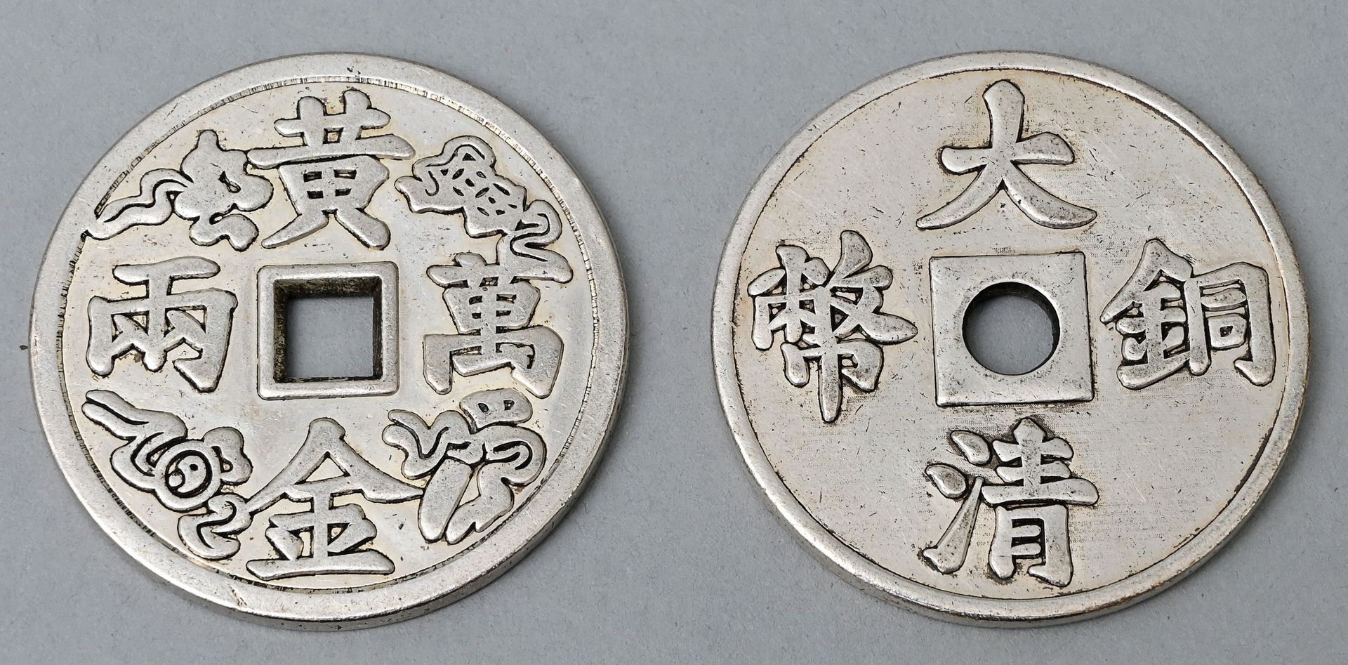 Null 两个亚洲硬币的复制品，20世纪的钢制。中间有方形或圆形孔的圆形硬币（模仿古老的奶酪硬币），上面刻有亚洲文字。在一个白色的小箱子里。D. 4,3 cm &hellip;