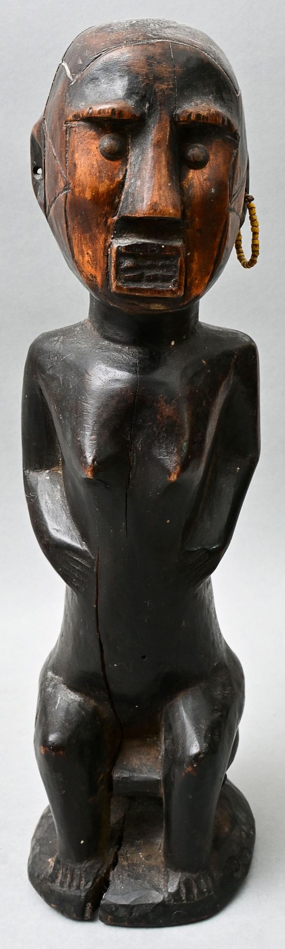 Null 雕像（祖先像），印度尼西亚，东帝汶（？ 女性形象坐在凳子上。木头，雕刻，深棕色和黑色的铜锈。墙纸钉子作为眼睛。一面是黄色玻璃珠的耳饰。由于年代久远而产&hellip;