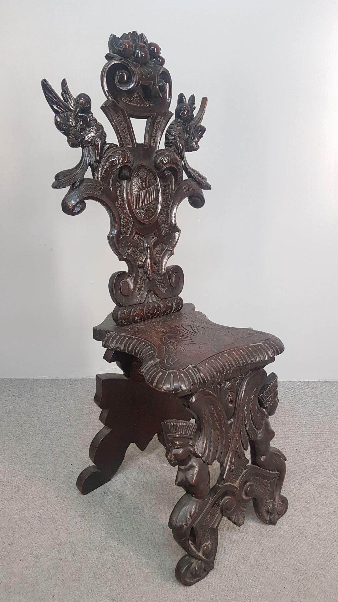 Null 一把发黑和染色的橡木效果的木椅，椅背上有丰富的鸟类、奖章和植被的雕刻装饰，正面底座上有翅膀的人物轮廓，座椅上有雕刻的图案。意大利作品，19-20世纪。&hellip;