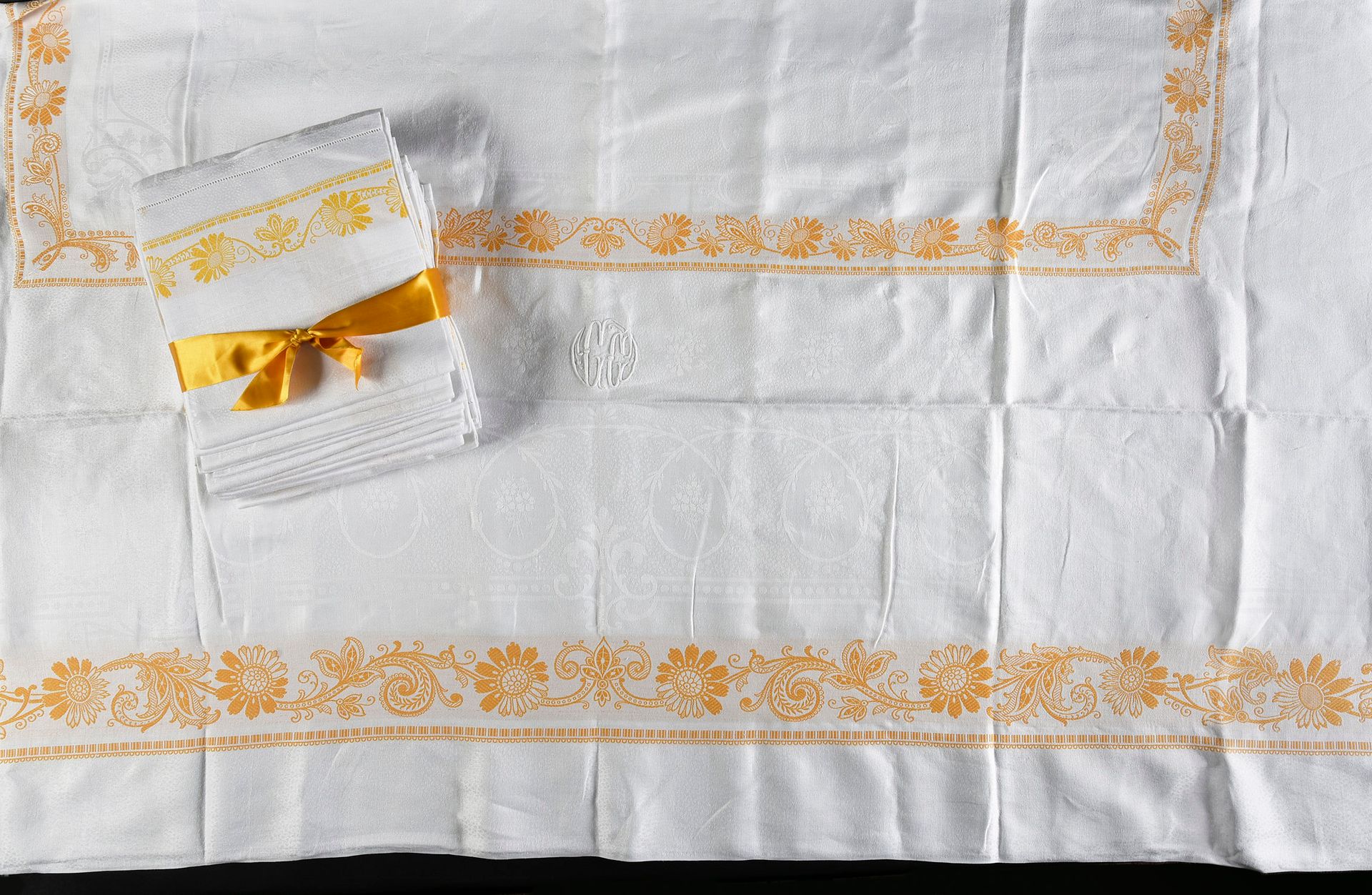 Null 桌布和18张餐巾，19世纪末。
桌布和18张餐巾，奶油色的棉质大马士革，上面有花卉装饰和对比鲜明的金黄色带状雏菊，数字GG用白色绣成。桌布尺寸：170&hellip;