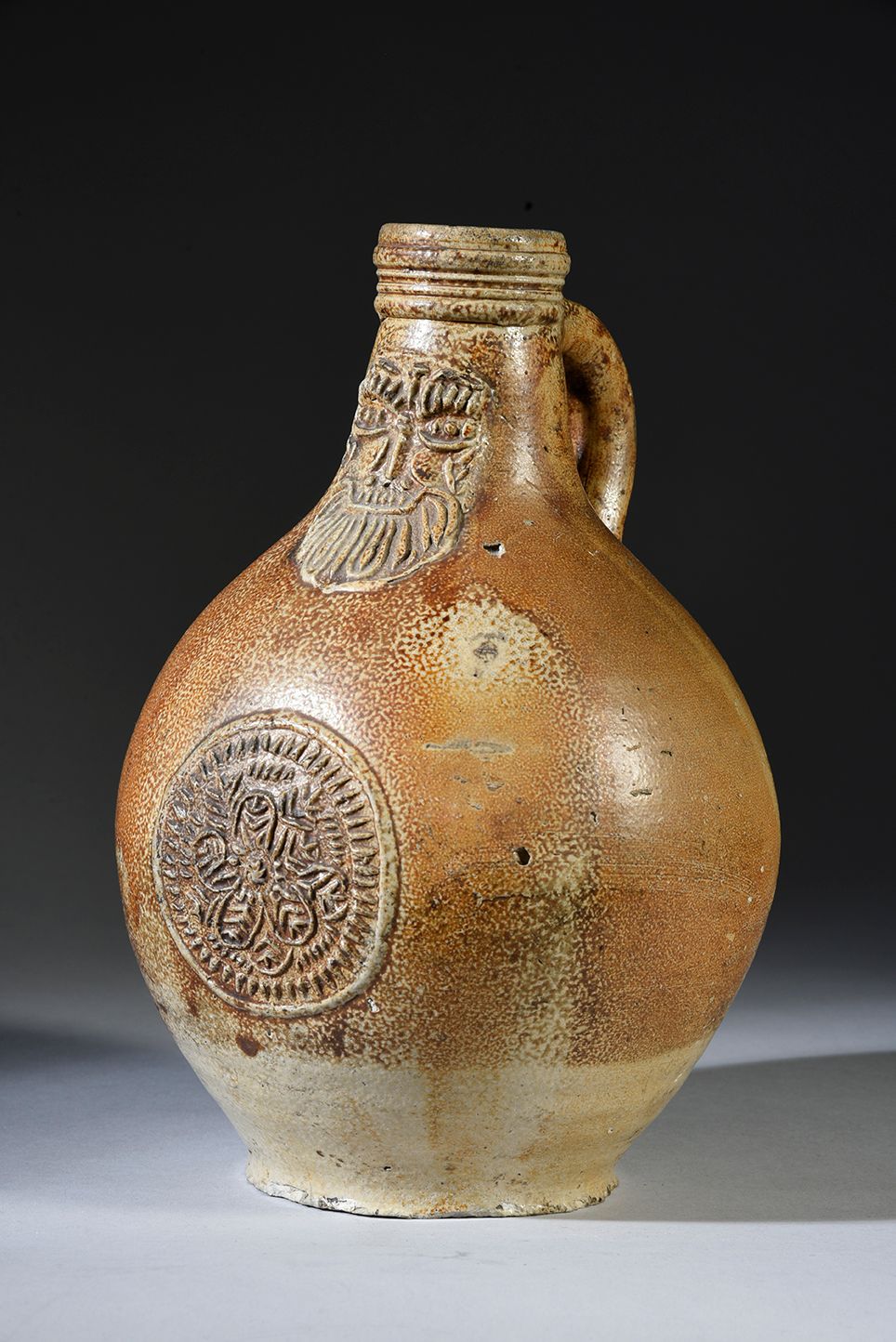Null 一件炻器球状体的瓶子，颈部装饰有一个大胡子的巴曼式的脸，瓶身有一个圆盘，上面有几何装饰和一朵花。
Frechen，约1600年
H.27 cm
(脚上&hellip;