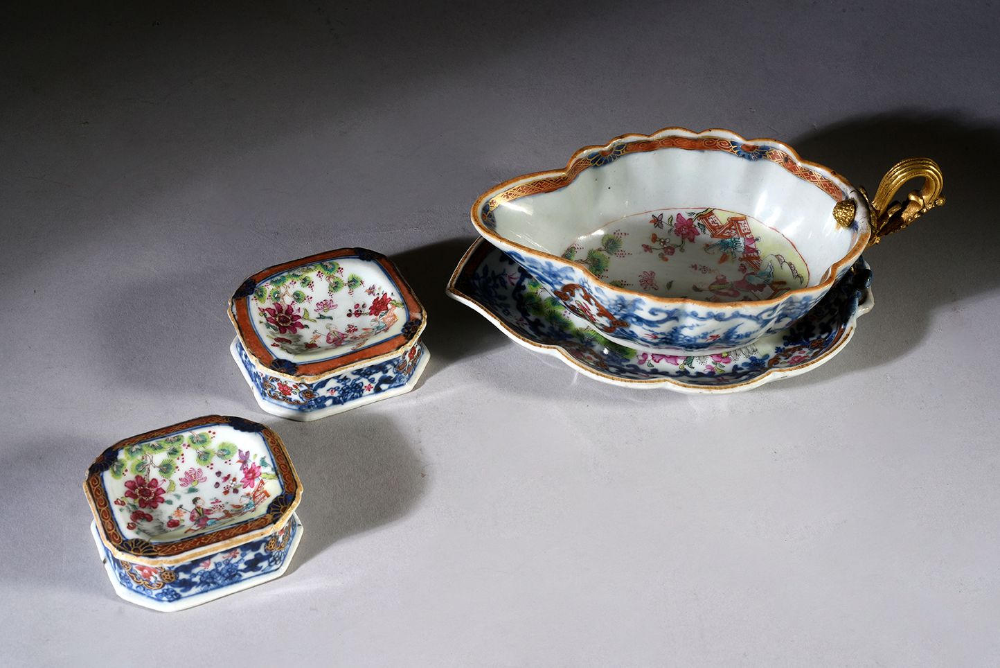 Null 一套中国瓷器装饰的人物叶子框架：
-一个水壶和它的托盘，手柄是铜制的，有凹凸不平的镀金装饰（19世纪的框架）。
长：18.5厘米
-两个长方形的盐渍碗&hellip;