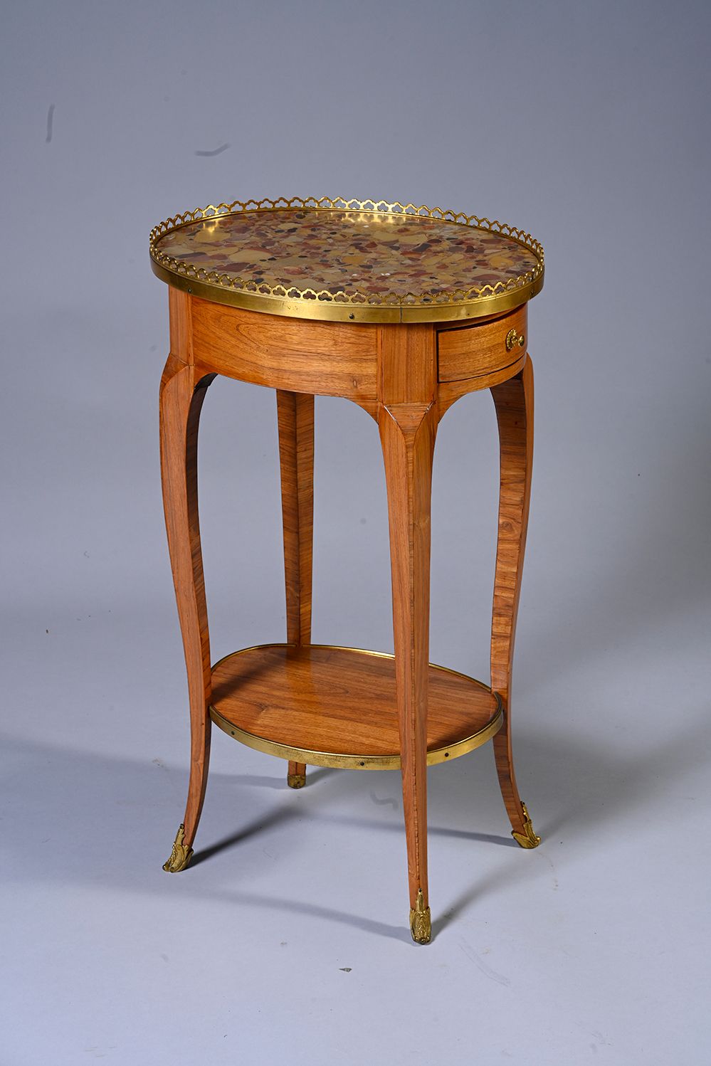 Null 一张红木贴面的椭圆形咖啡桌，上面有Breche d'Alep大理石。 它在腰部有一个侧边的抽屉，在四个弯曲的腿上有一个支架架。饰有镀金的青铜器。
路易&hellip;