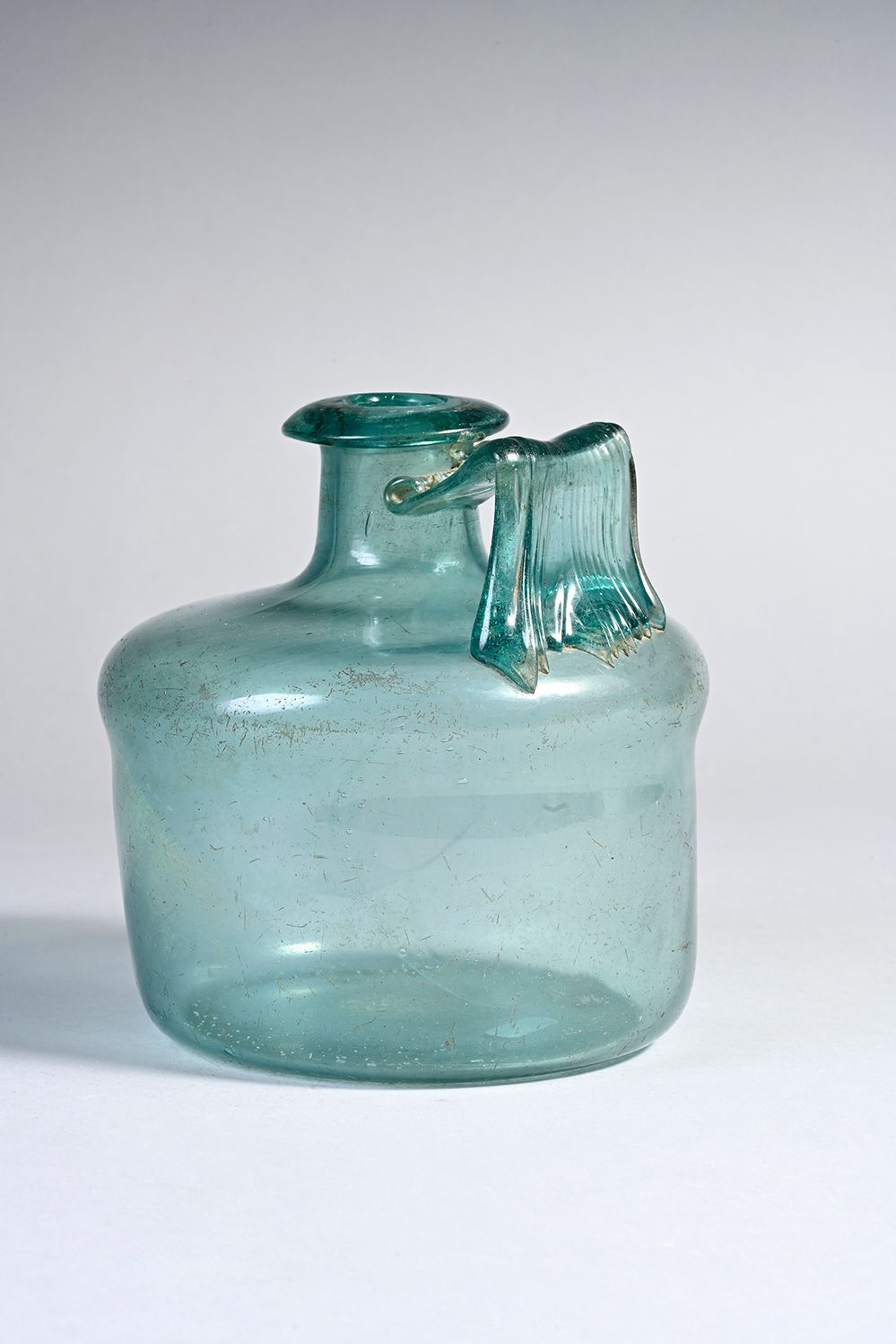 Null 瓶身为圆柱形，带状手柄。蓝绿色的玻璃。
加洛-罗马艺术，1-3世纪。
完好无损。高13.5厘米。