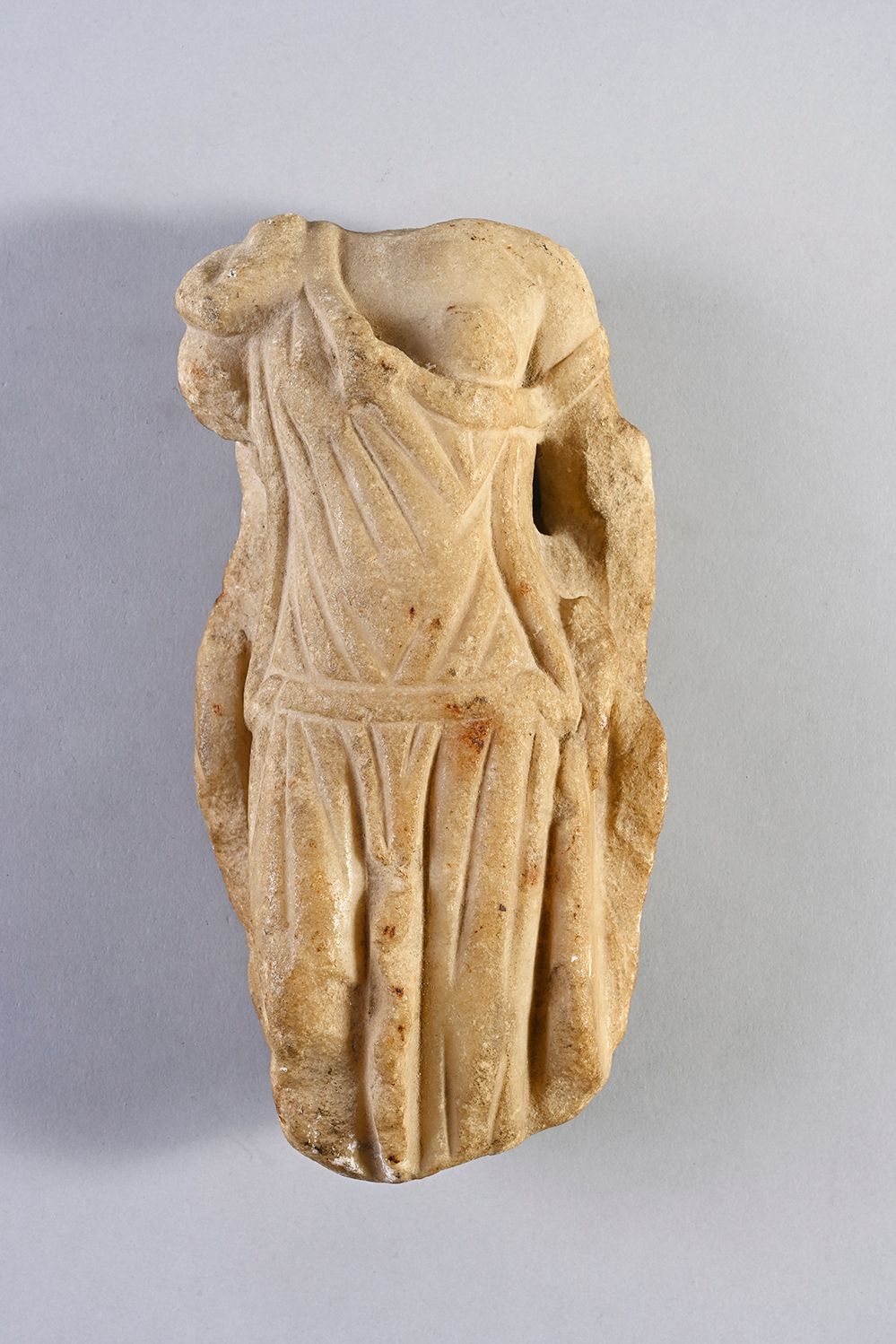 Null 残缺的女性雕像，无头，身穿腰间束紧的披肩，露出左胸。白色大理石。米色的深度着色。可见的漏洞。
罗马艺术，3世纪。
H.20厘米。