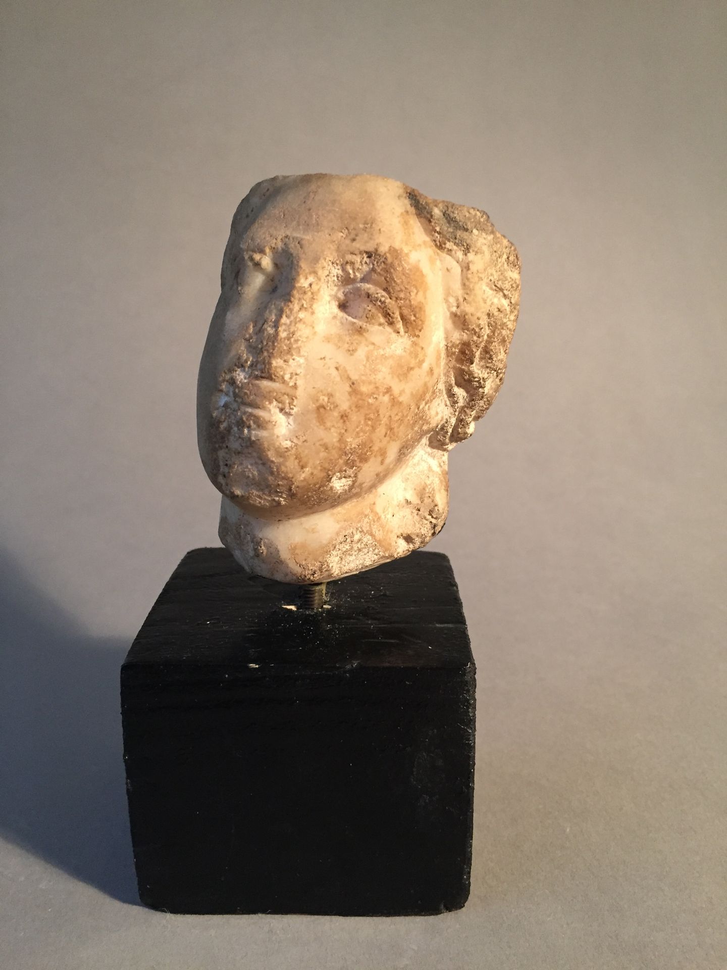 Null 女性头像，头发在脖子后面聚成一个发髻。眼睛的细节很精致。白色大理石。可见的漏洞。石灰岩矿床。罗马艺术，1-2世纪。高8厘米。