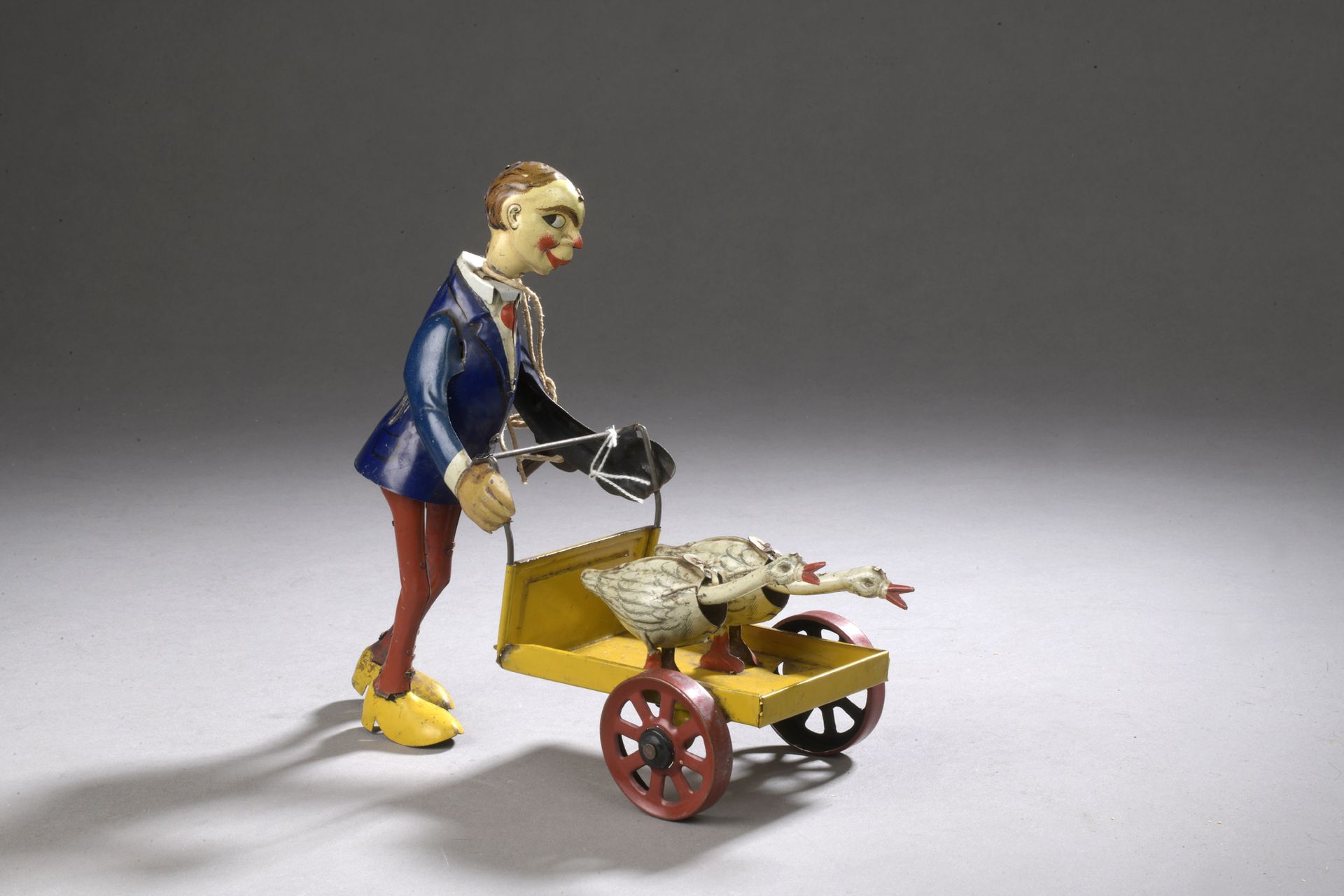 Null FISCHER, 1920 - 机械玩具，有一个推着车的人物，车上有两只鹅。彩绘和平版印刷的金属板。

19 x 18 cm