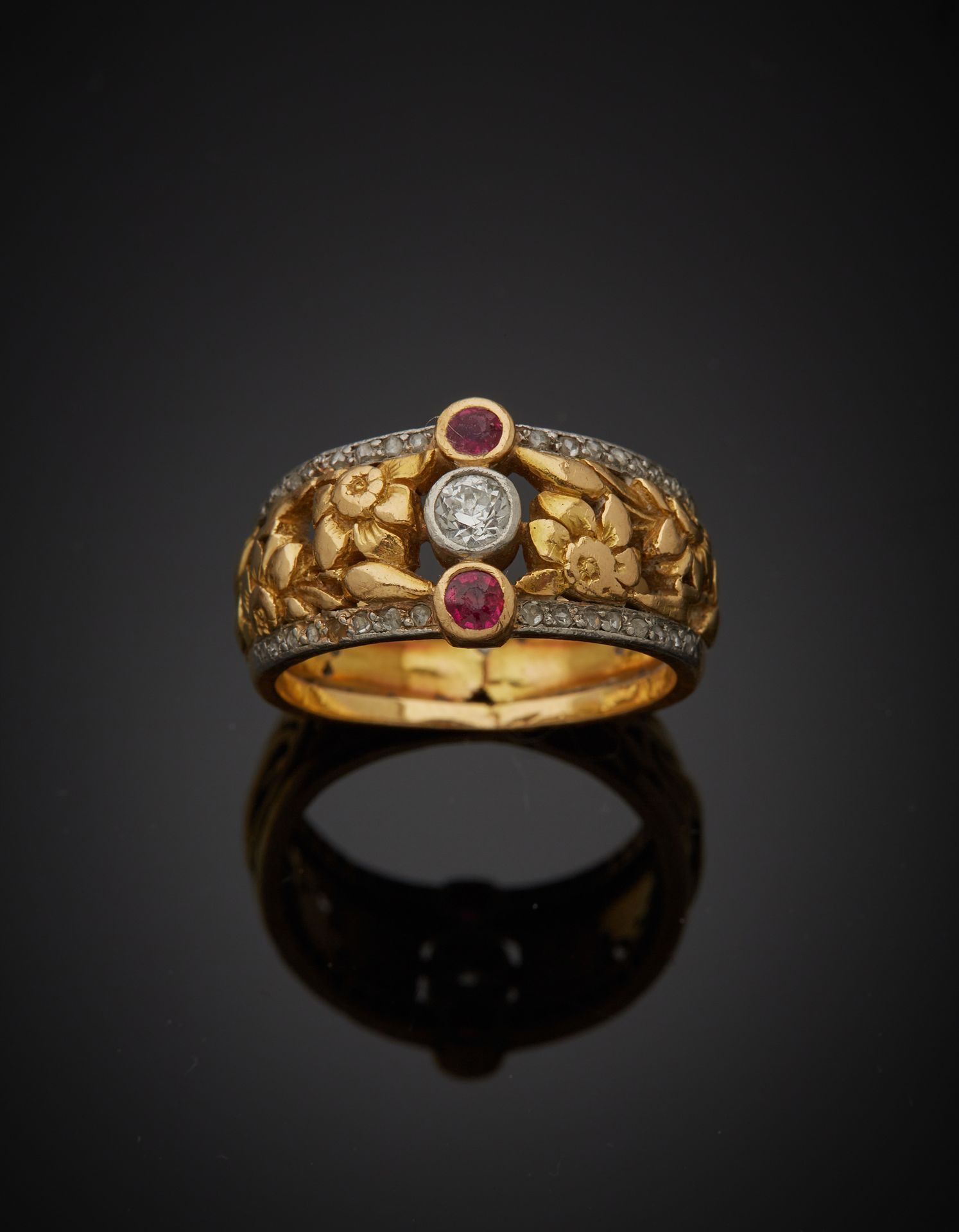 Null 一枚18K 750‰的双色金带戒指，中央是一颗明亮式切割的钻石，肩部是两颗红色的宝石，戒指上刺有花纹，并有玫瑰式切割钻石的线条勾勒。这些石头有的破碎，&hellip;