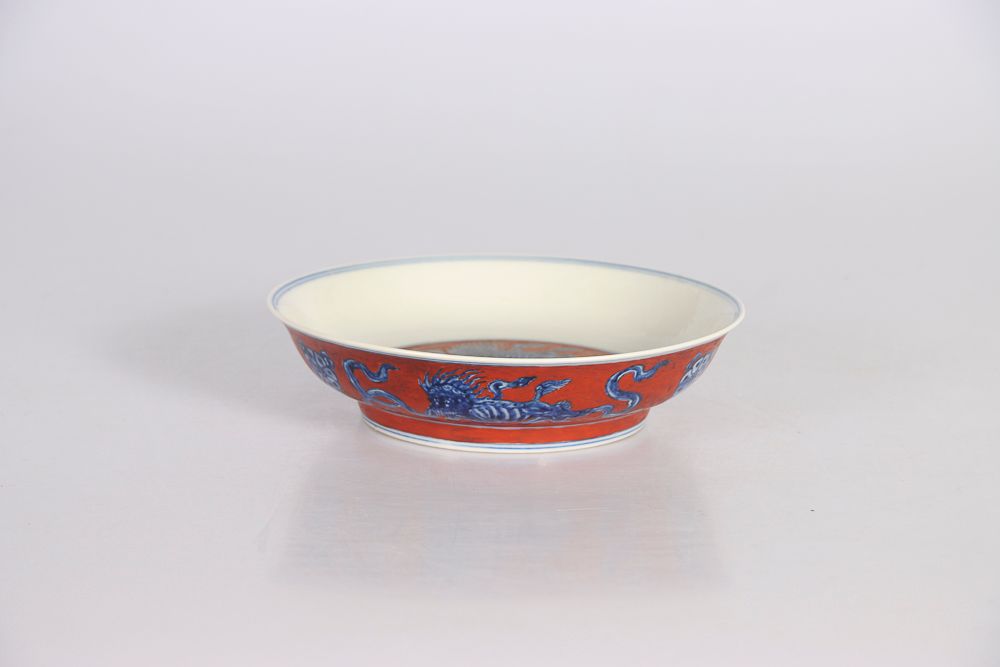 Null 中国，18世纪或更早。瓷盘上有钴蓝和铁红的装饰，三只能犬在玩锦绣球。底下有釉里红双圈内的 "成化 "六字款。D : 18,8 cm (底部有小的修复)