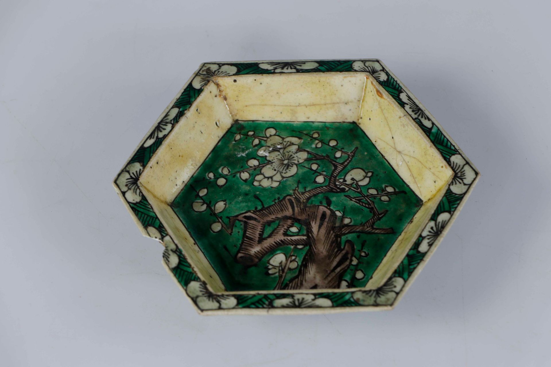 Null *中国，康熙时期，18世纪。六角形的瓷盘，一面用绿色的家传珐琅彩装饰着盛开的梅花枝，外壁有佛教纹饰。背面有墨色的灵芝标记，还有一个旧标签。长 : 11&hellip;