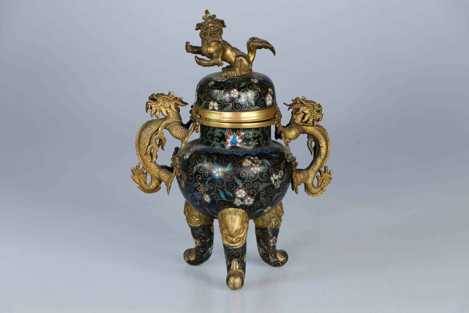 Null 中国，19世纪。鎏金铜合金和黑底多色掐丝珐琅覆盖的鼎形香炉，安装在三个奇美拉头形的弯腿上，圆拱形的炉身饰有轮圈和花朵，把手为龙形。盖子是佛教狮子的形状&hellip;