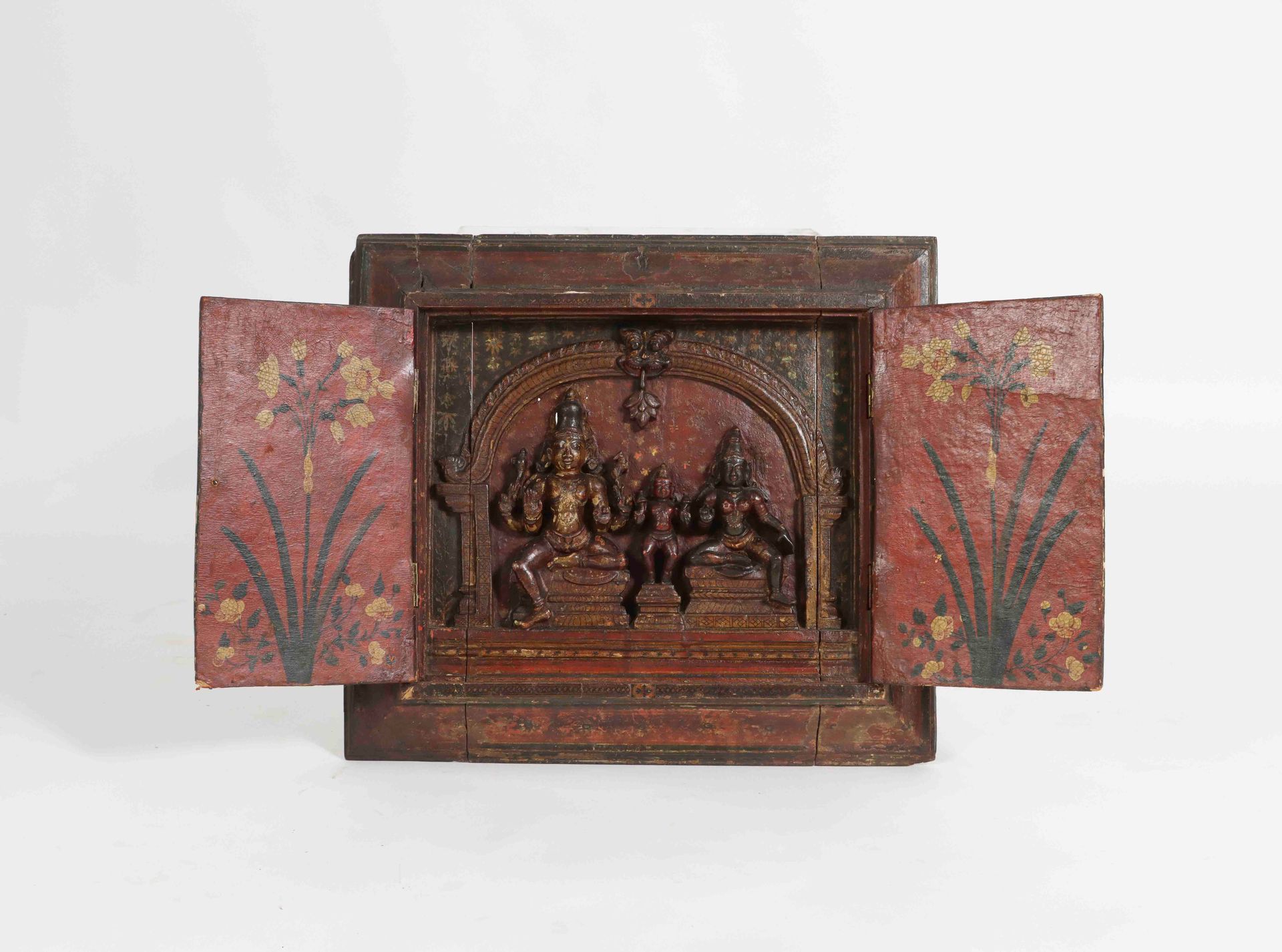 Null 印度，18-19世纪。一件罕见的涂漆和镀金的木质宗教祭坛画，带有花卉装饰，被放在一个由两扇门打开的框架中。它显示了一个雕刻的三神场景（事故和缺失的部分&hellip;