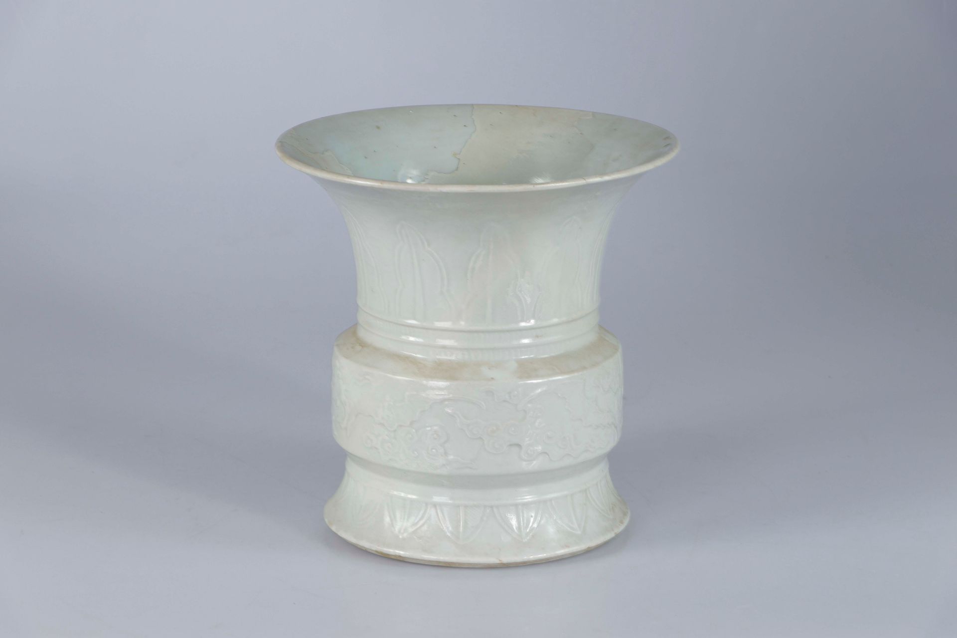 Null 中国，18世纪。白色单色瓷器中的古铜器形式的 "古 "字型角瓶，边缘有蝙蝠在云间飞翔的图案，颈部和底部有香蕉叶楣的衬托。高：25.5；深：26厘米（事&hellip;
