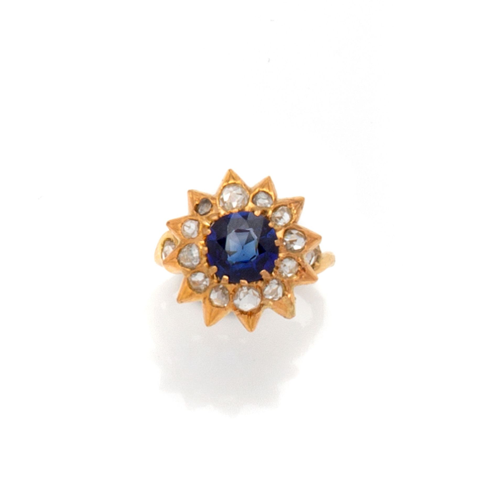 Null 18K（750/1000）黄金戒指，以爪式镶嵌的圆形蓝宝石为中心的雏菊设计；每个花瓣都镶嵌着一颗玫瑰切割钻石。戒指以两颗明亮式切割钻石的封闭式镶嵌完成&hellip;