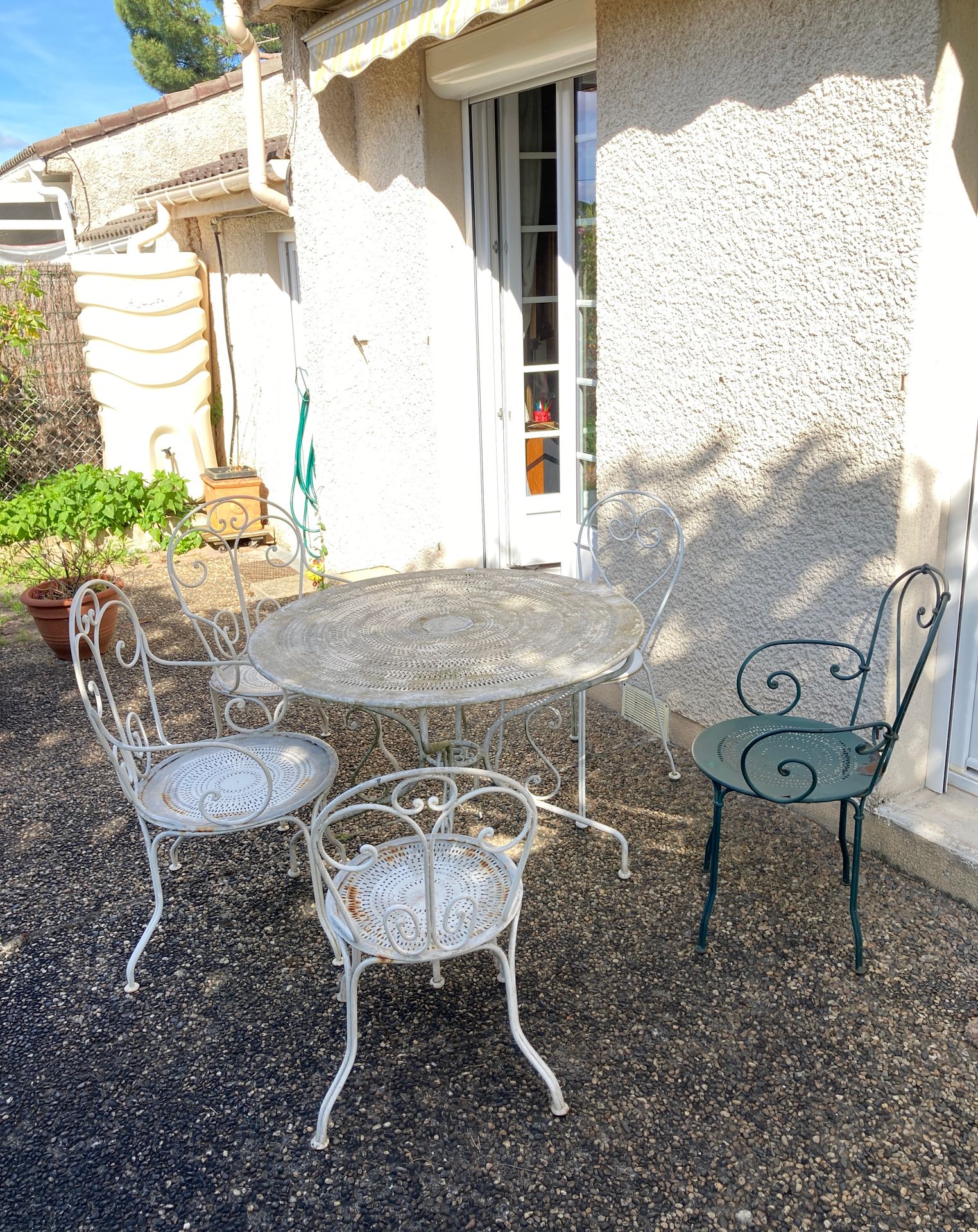 Une table en métal laqué blanc, trois fauteuils et deux chaises, dont une verte.