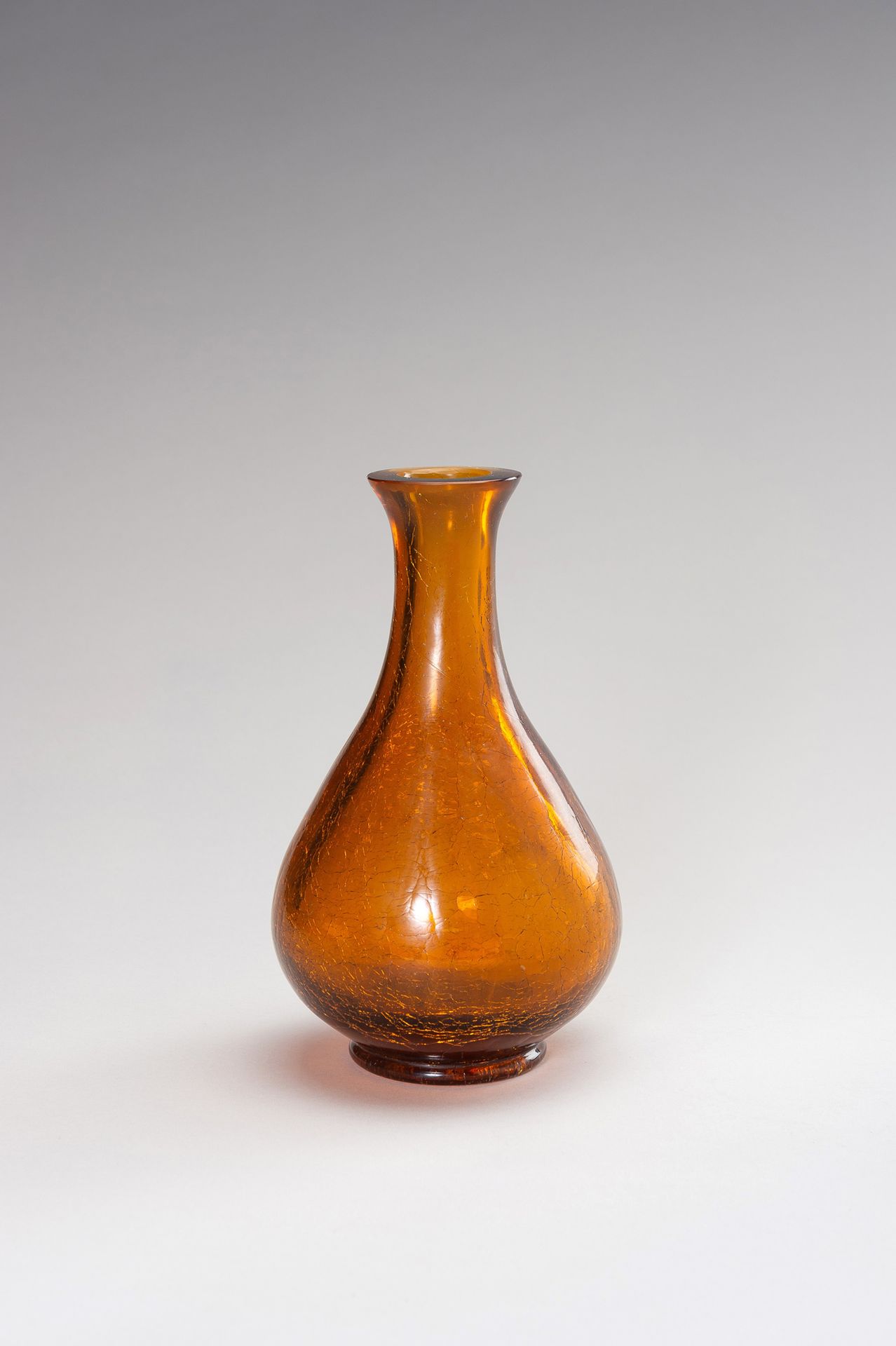 AN AMBER CRACKLE GLASS VASE 一个琥珀色的裂纹玻璃瓶
中国，清末（1644-1912）。透明的琥珀色玻璃花瓶是梨形的，从短底上升到腰部&hellip;