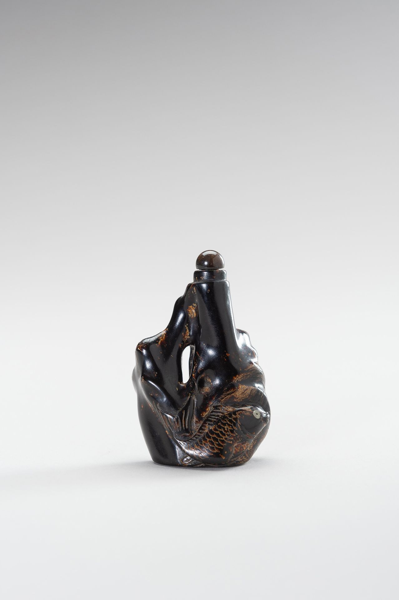 A BLACK CORAL SNUFF BOTTLE 黑珊瑚鼻烟壶
中国，清末（1644-1912）。精致的瓶子符合珊瑚枝的自然轮廓，雕有一条大鲤鱼，鱼眼镶嵌在&hellip;