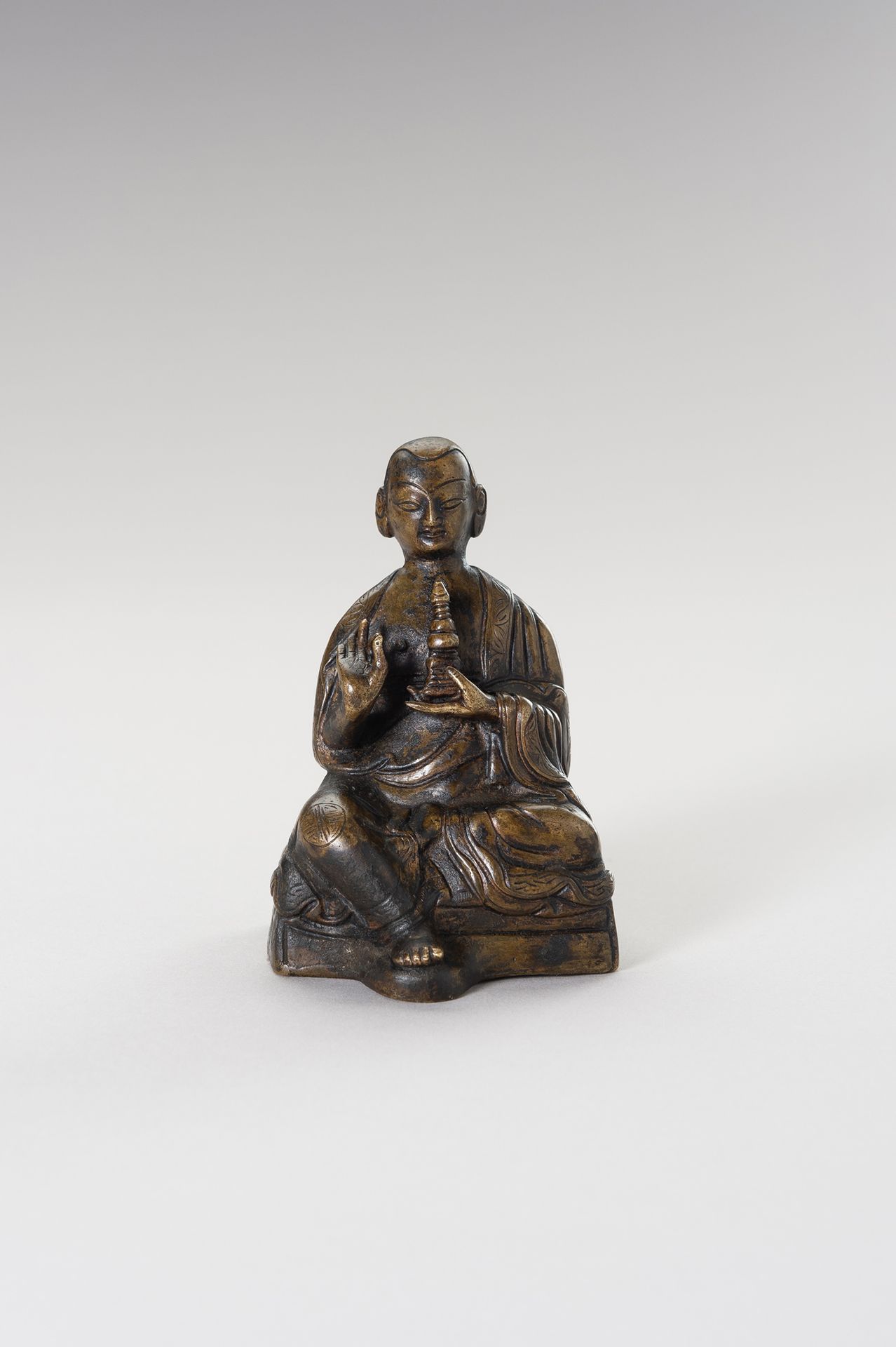 A Bronze figure of a Lama 喇嘛铜像
西藏，19 世纪。喇嘛坐着，右手拿着维拉卡穆德，左手拿着佛塔，袈裟上有雕刻的边框。脸部表情安详，杏&hellip;