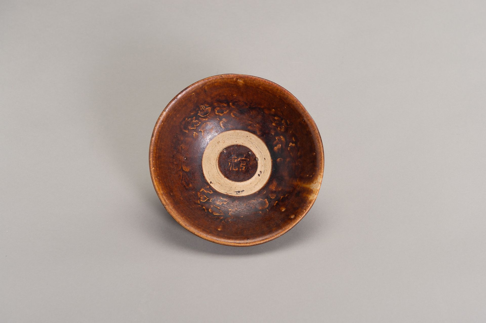 A BROWN GLAZED MOLDED BOWL 一个棕色釉面模制的碗
中国，明朝（1368-1644）。深圆的侧面从短直的底上升到略微弯曲的边缘，内部两侧&hellip;