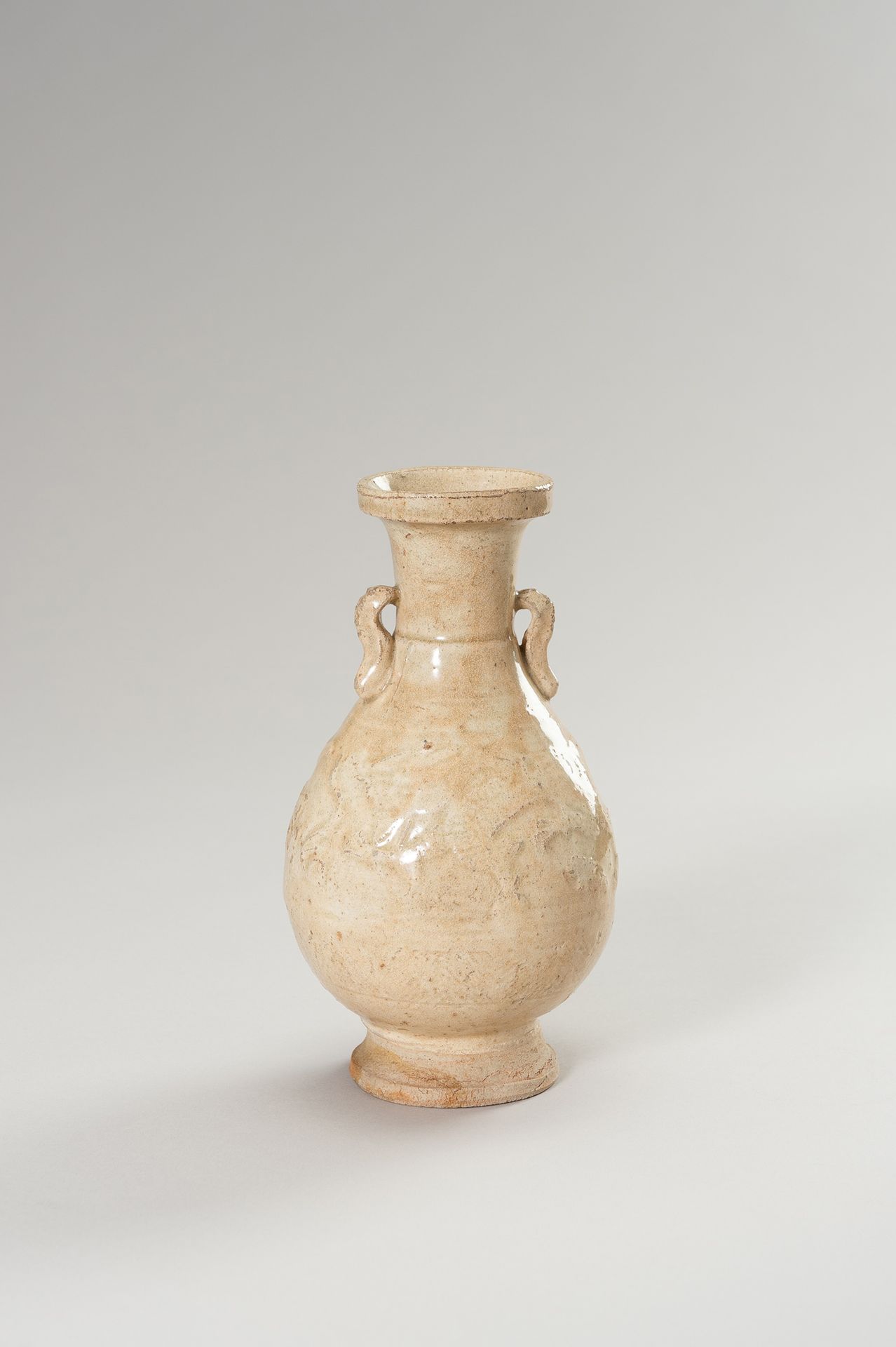 A BEIGE GLAZED CERAMIC VASE 灰色釉面陶瓷花瓶
中国，元朝（1271-1368）。梨形的瓶身在一个弯曲的圆柱形底上，颈部有一个碟形的边&hellip;