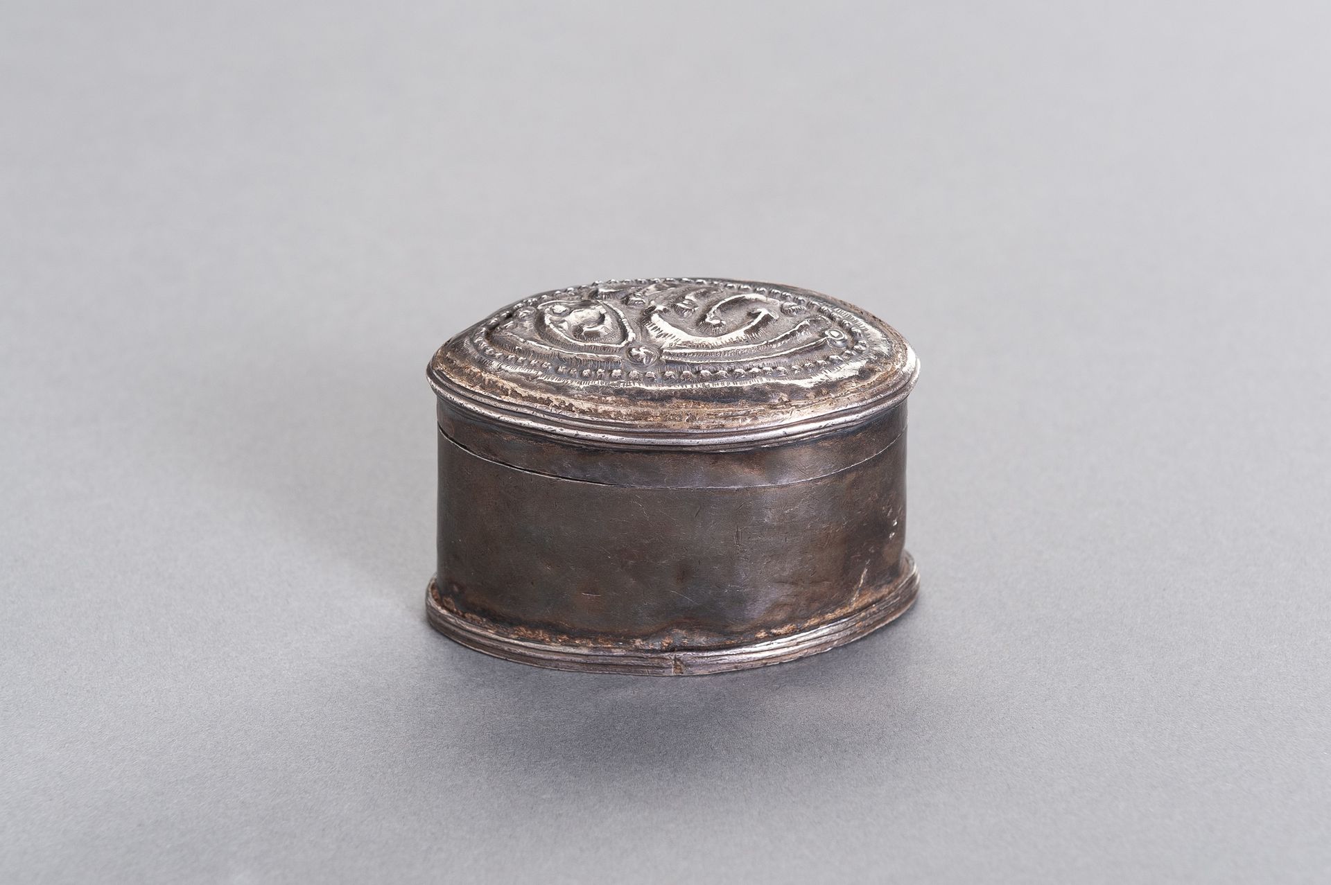 AN OVAL-SHAPED SILVER MEDICINE BOX 椭圆形银质药箱
缅甸/缅甸，19世纪。椭圆形的银盒盖上有精美的浮雕图案。

状况。有凹痕，&hellip;