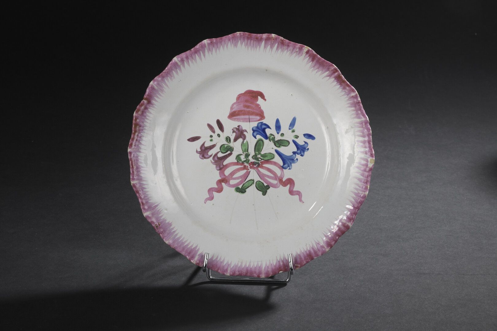 Null LES ISLETTES，18世纪

多色陶盘上装饰着一束百合花，上面有一顶由蝴蝶结托着的弗里吉亚帽。梳理的边缘。

小碎片。

D. 22,2厘米