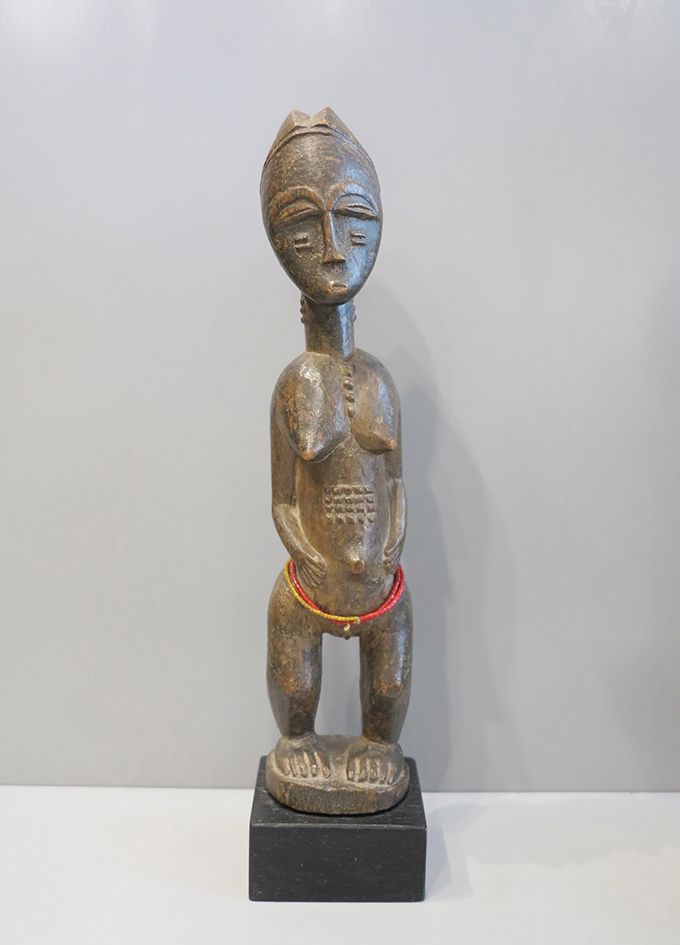 Maternité Baoulé 孕妇雕像站在一个小的圆形平台上，手臂放在两侧，双手放在突出的脐部两侧。腹部和突出的乳房之间的瘢痕疙瘩，颈部两侧和脸颊以及下背部&hellip;