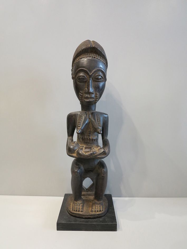 Maternité Baoulé 精雕细琢的母性雕像，描绘的是坐在凳子上和圆形露台上，怀里抱着她的孩子。突出的乳房、嘴唇周围、腹部和背部的瘢痕疙瘩。徽章的发型以&hellip;