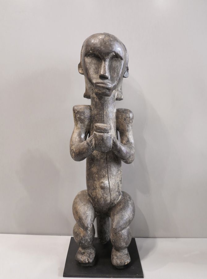 STATUE FANG 拟人化的雕像，一个坐着的女人，两只手拿着一个杯子，头饰由中间的山脊划定。木头有略微发亮的铜锈。

加蓬，芳族

17x17x60厘米