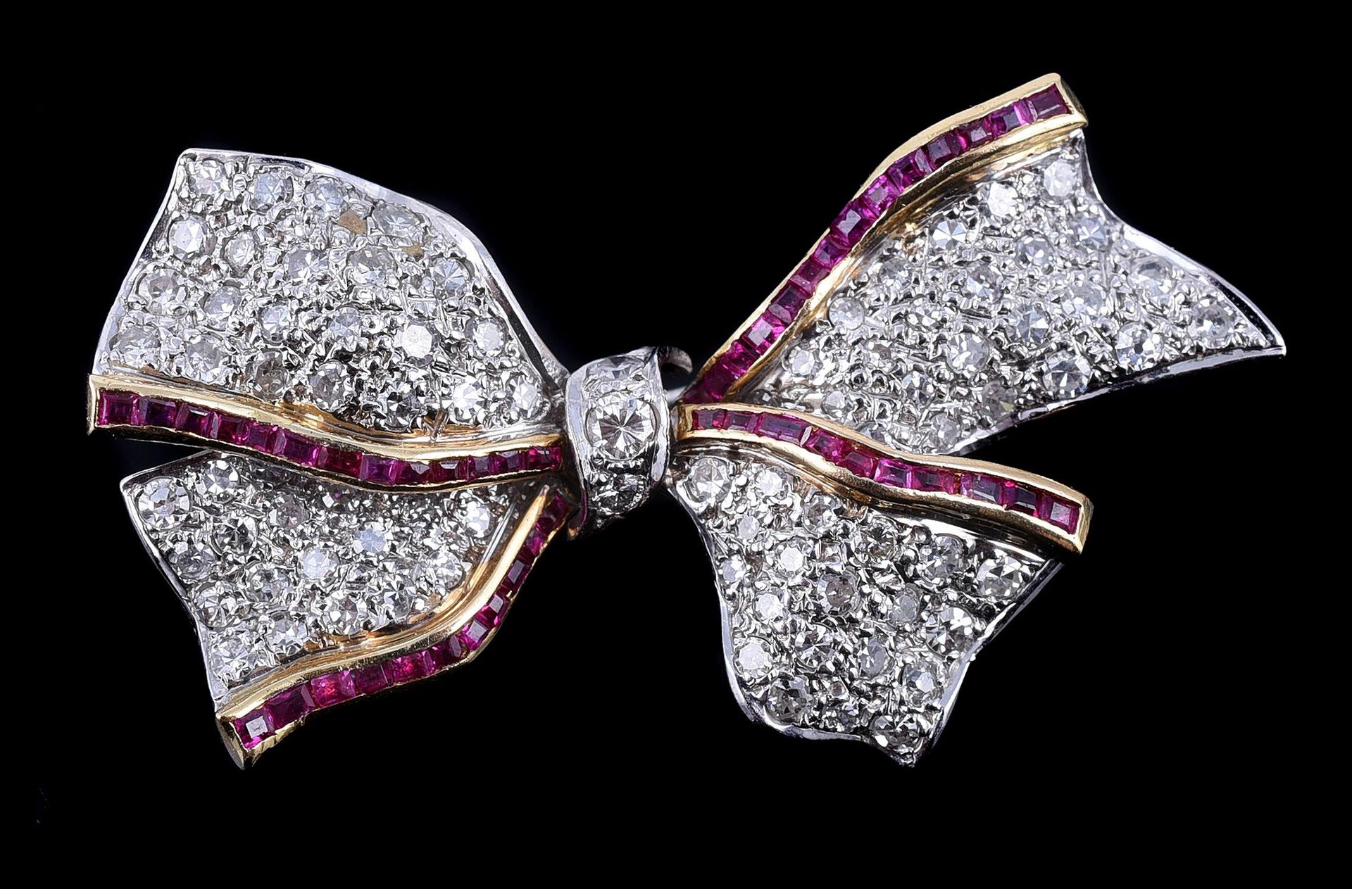 A ruby and diamond bow brooch 一枚红宝石和钻石蝴蝶结胸针，交叉的锥形面板上密镶了8颗切割钻石，总重约1.00克拉，并有通道镶嵌的红&hellip;