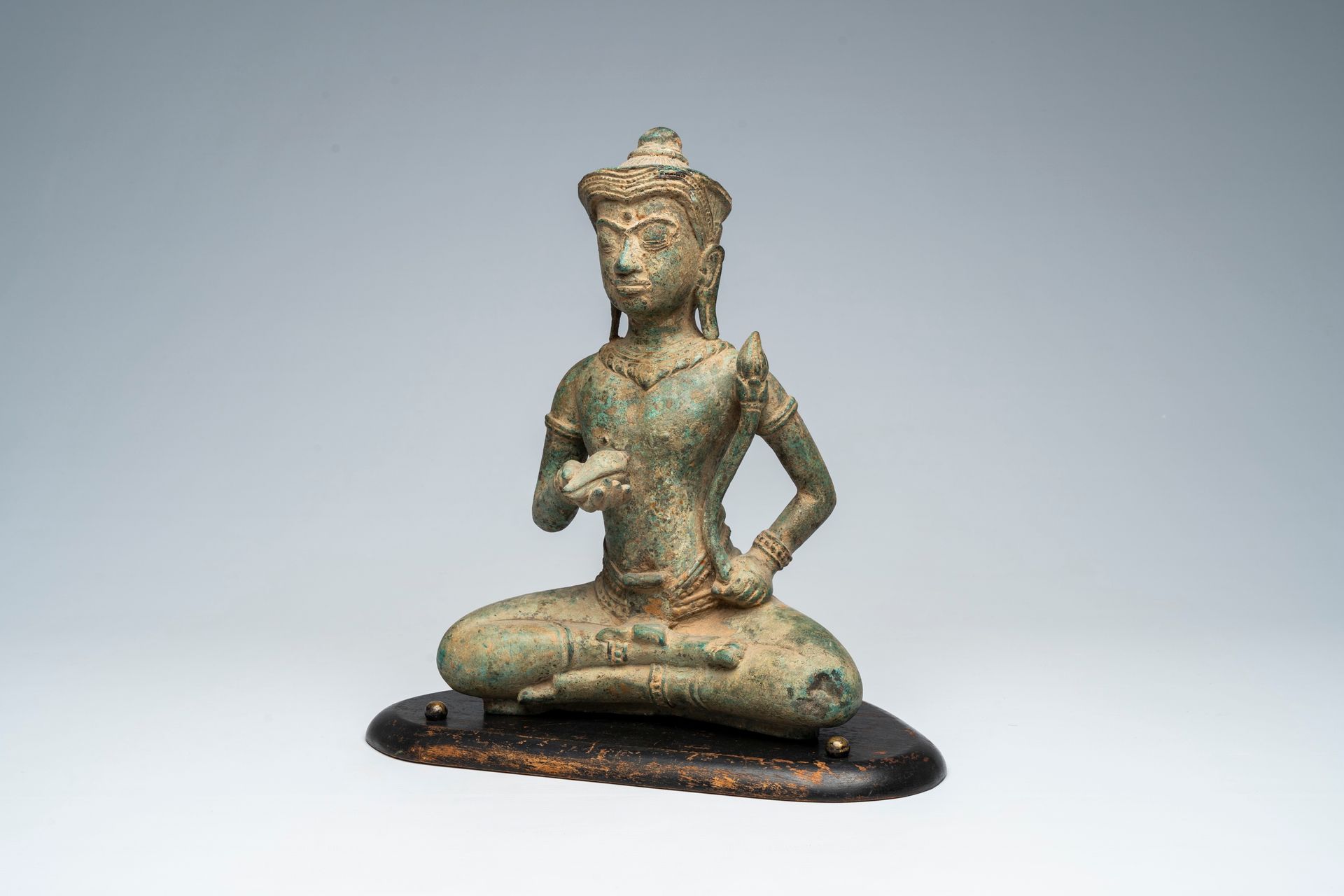 A bronze figure of a seated deity with a shell and a lotus flower in the hands, &hellip;