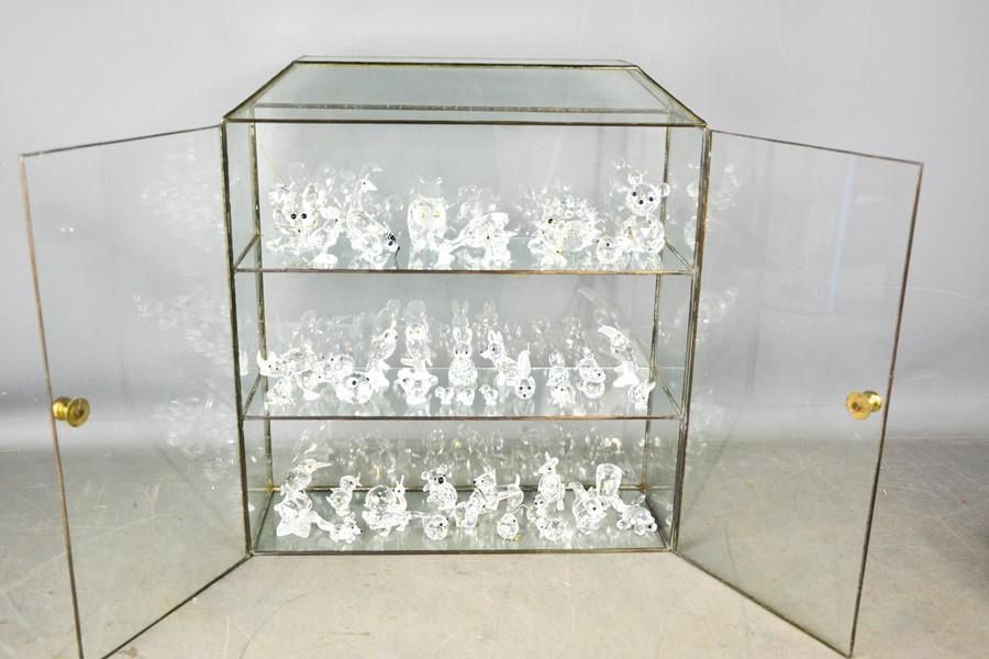 Null A glass display cabinet, together with a group of Swarovski crystal animal &hellip;