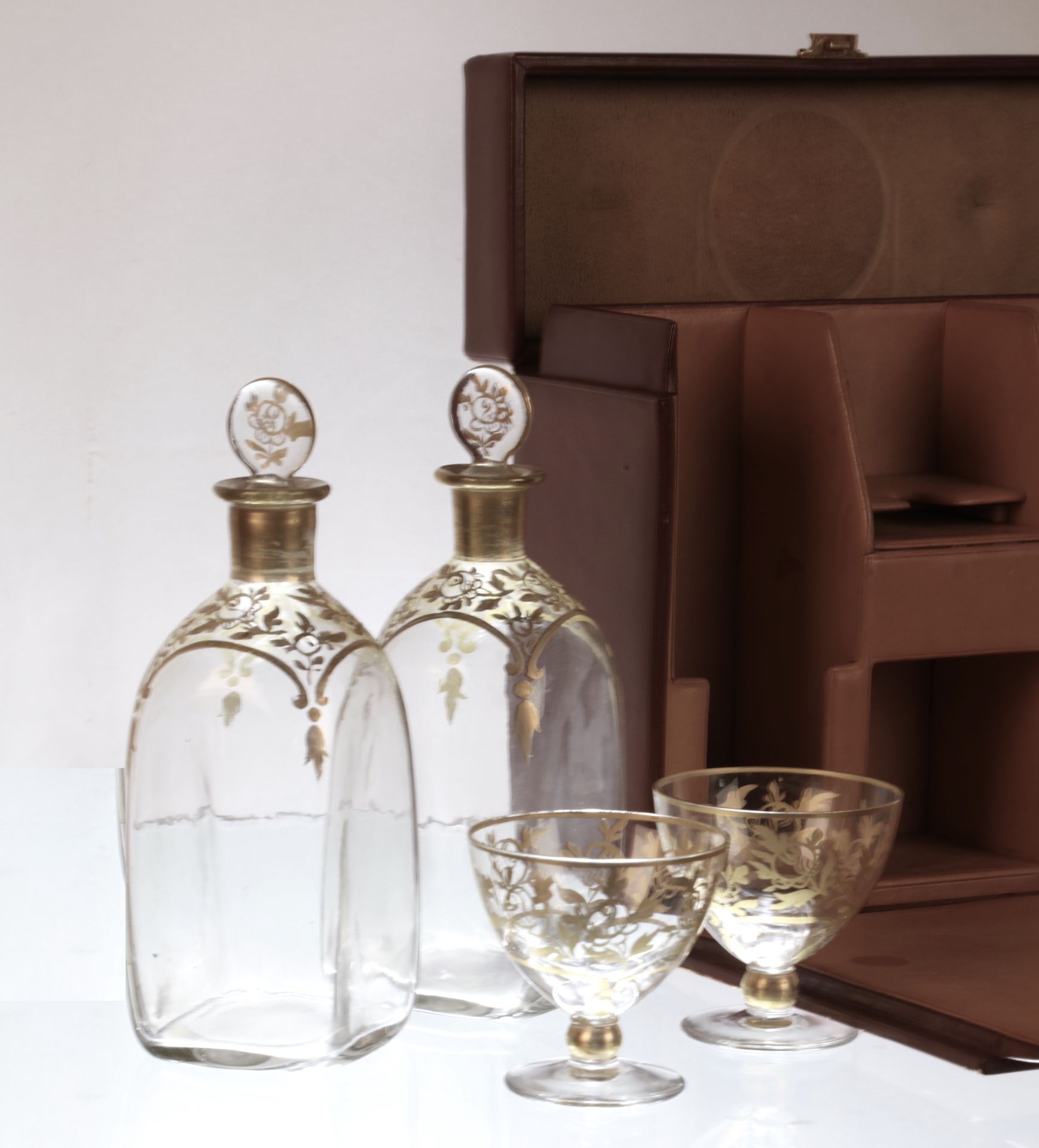 Null 
棕色皮革酒柜，露出两个带瓶塞的吹制玻璃瓶，还有两个小杯子，有镀金装饰。