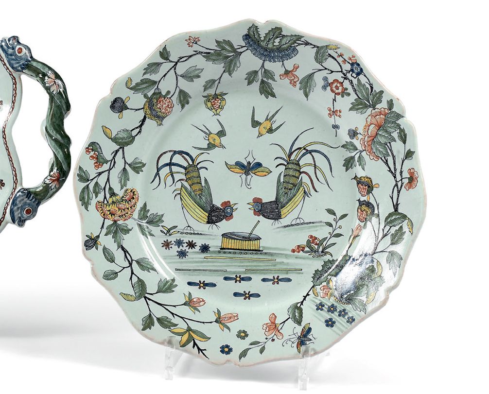 ROUEN 盘子有轮廓的边缘，多色的装饰，中间是两只公鸡围着一个盆子，上面是两只鸟和一只蝴蝶，在大树枝的翅膀上装饰着康乃馨、鲜花和石榴。
18世纪。
直径：24&hellip;