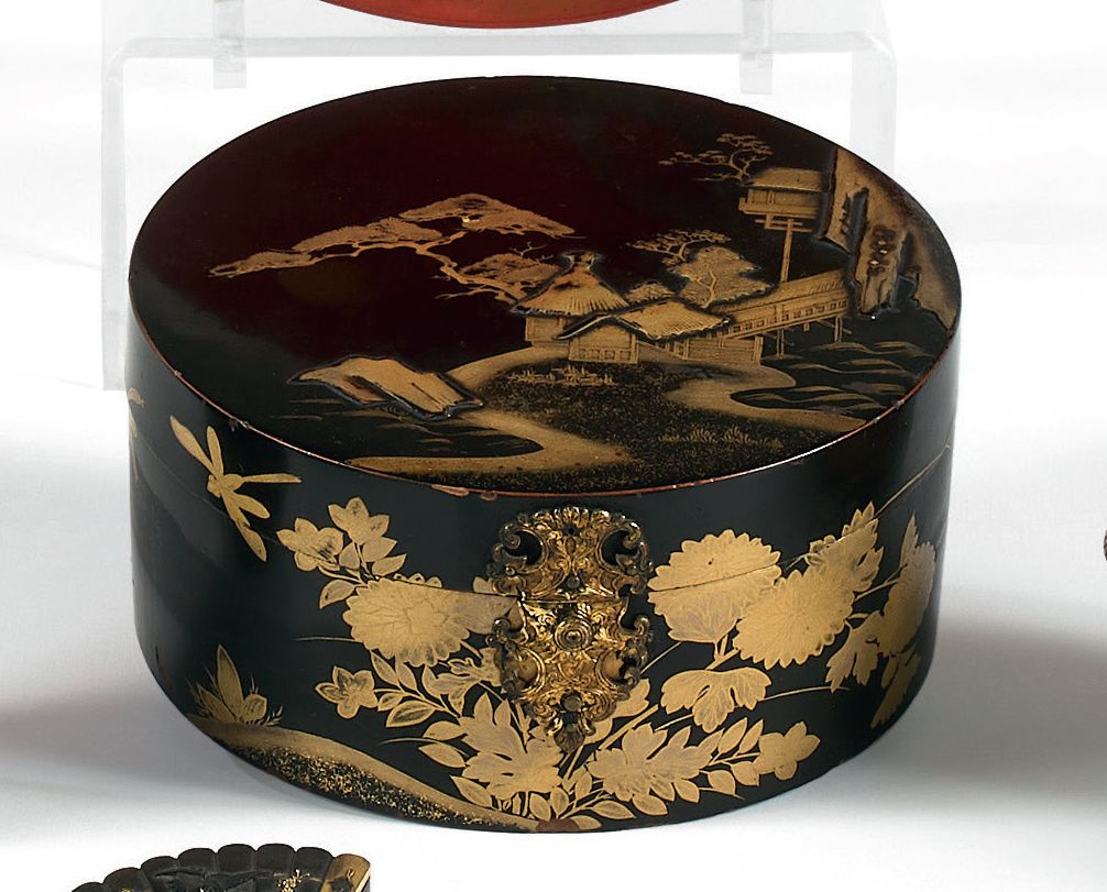 Null 一个日本漆器圆柱形有盖盒，黑色背景，金色的山水、宝塔和蝴蝶的装饰。内部有一个冒险的背景，凿刻和鎏金的铜锁和铰链。
18世纪初。
高度：7厘米 - 直径&hellip;