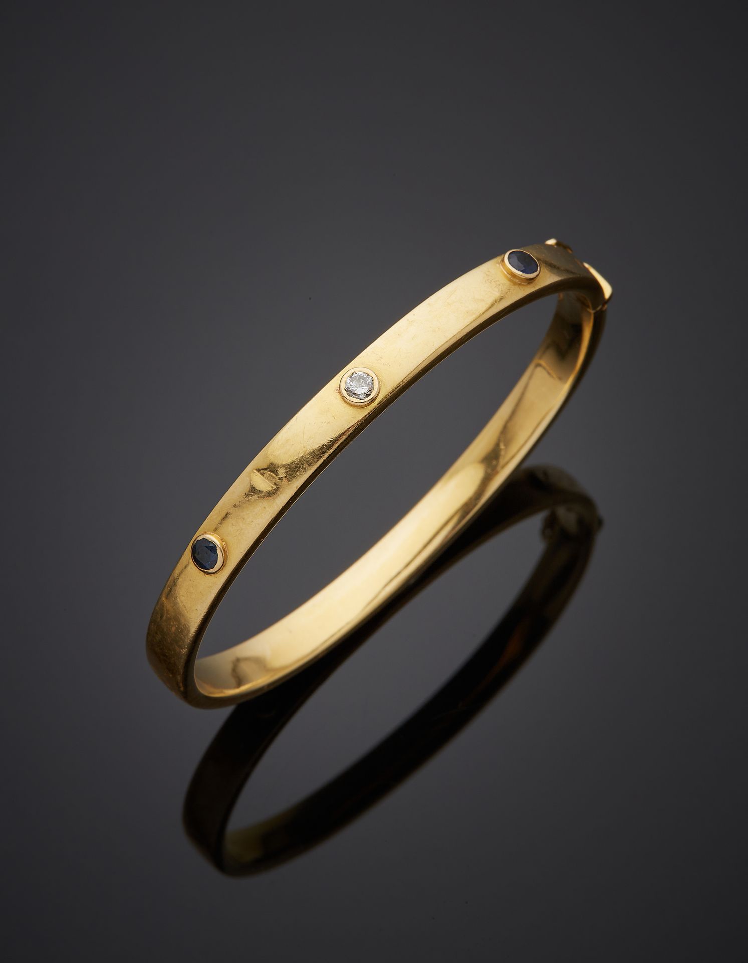 Null 黄金（750‰）开口刚性手镯，有三个螺丝图案，镶嵌两颗蓝宝石和一颗明亮型切割钻石。轻微的震动。
长度：18厘米。毛重：18克。