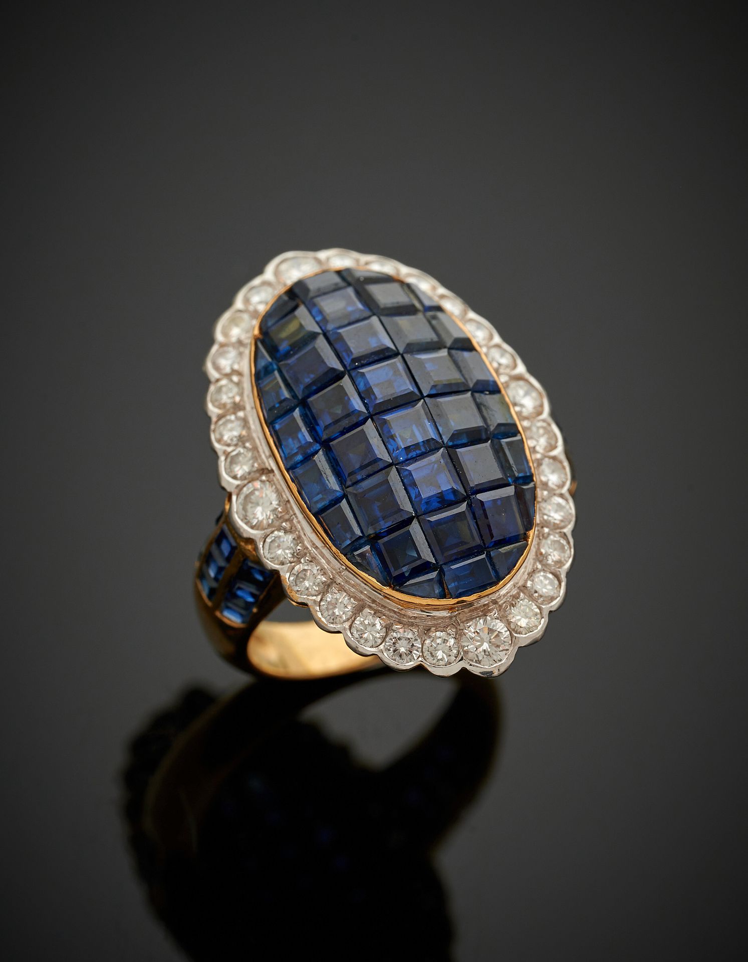 Null 重要的椭圆形白金和黄金(750‰)戒指，以隐形方式镶嵌校准蓝宝石，周围是明亮式切割钻石，肩部是三条校准蓝宝石的排列。 
手指：56。设计尺寸：2.8 &hellip;