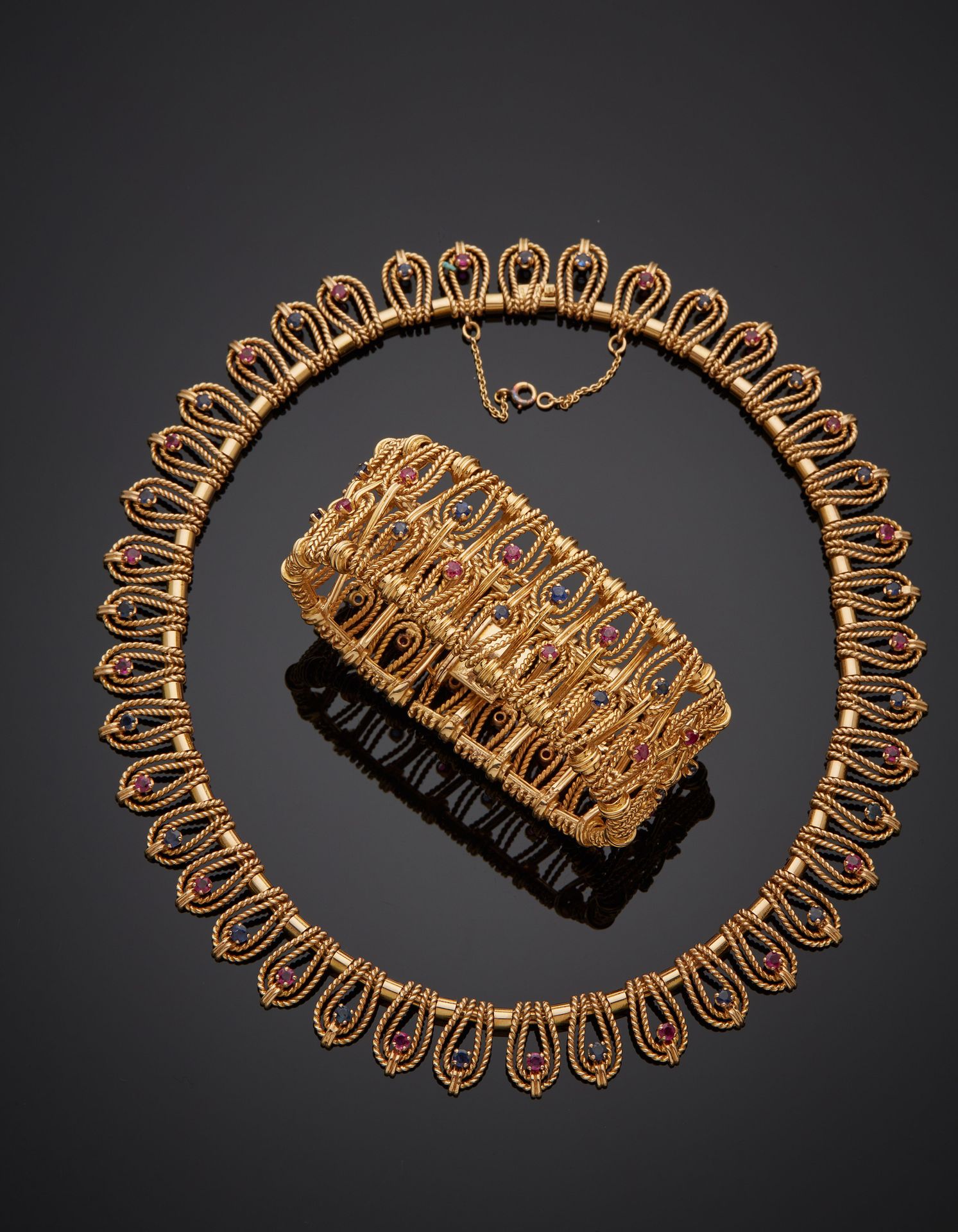 Null 一件 "流苏 "半宝石项链，由颈链和宽袖口手镯组成，黄金（750‰），镂空，扭曲，有水滴图案，镶嵌蓝宝石和粉色宝石，。
法国作品，约1960年。
项链&hellip;