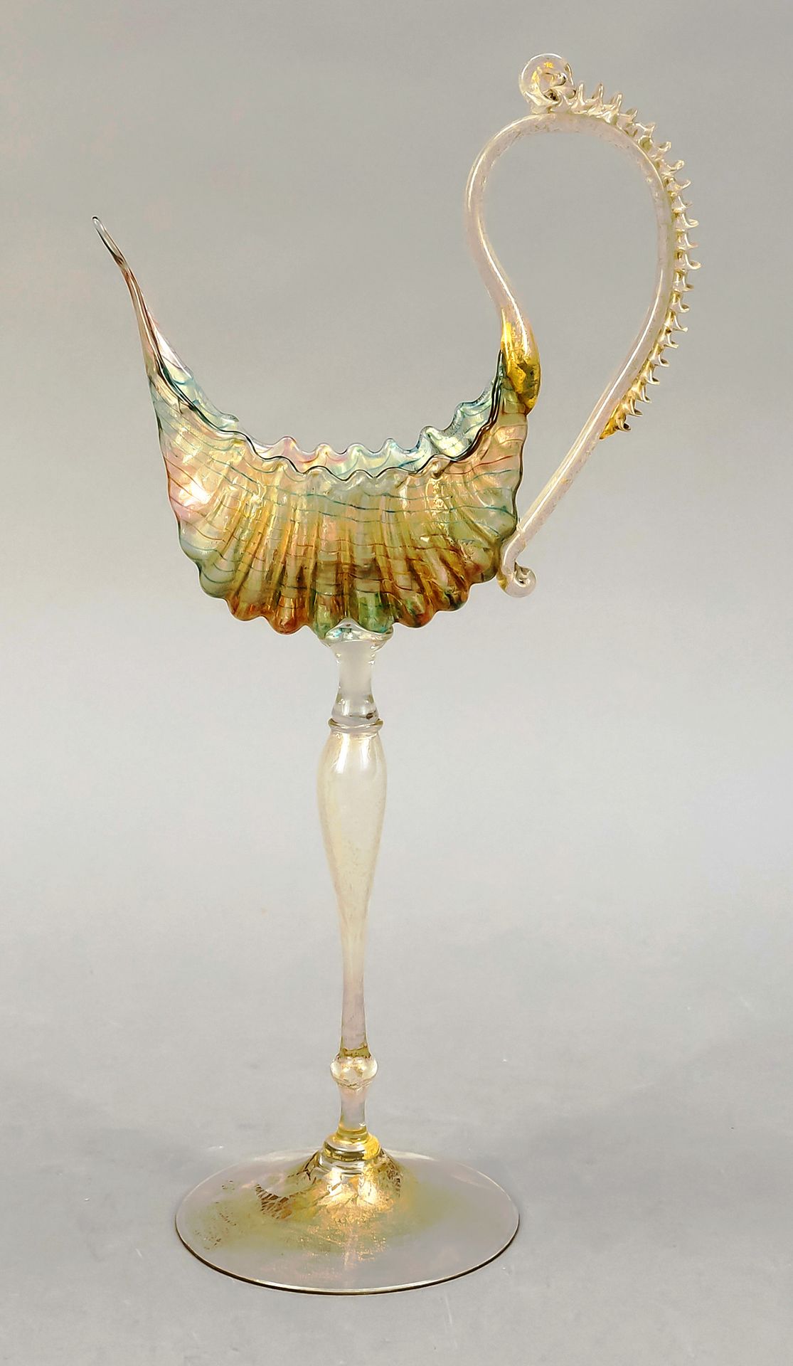 Null 装饰性高脚杯，意大利，20世纪下半叶，穆拉诺，鹦鹉螺高脚杯的风格，圆形圆盘底座，细长的轴，主体是一个风格化的贝壳形状，侧面有延伸的把手，透明玻璃上有绿&hellip;