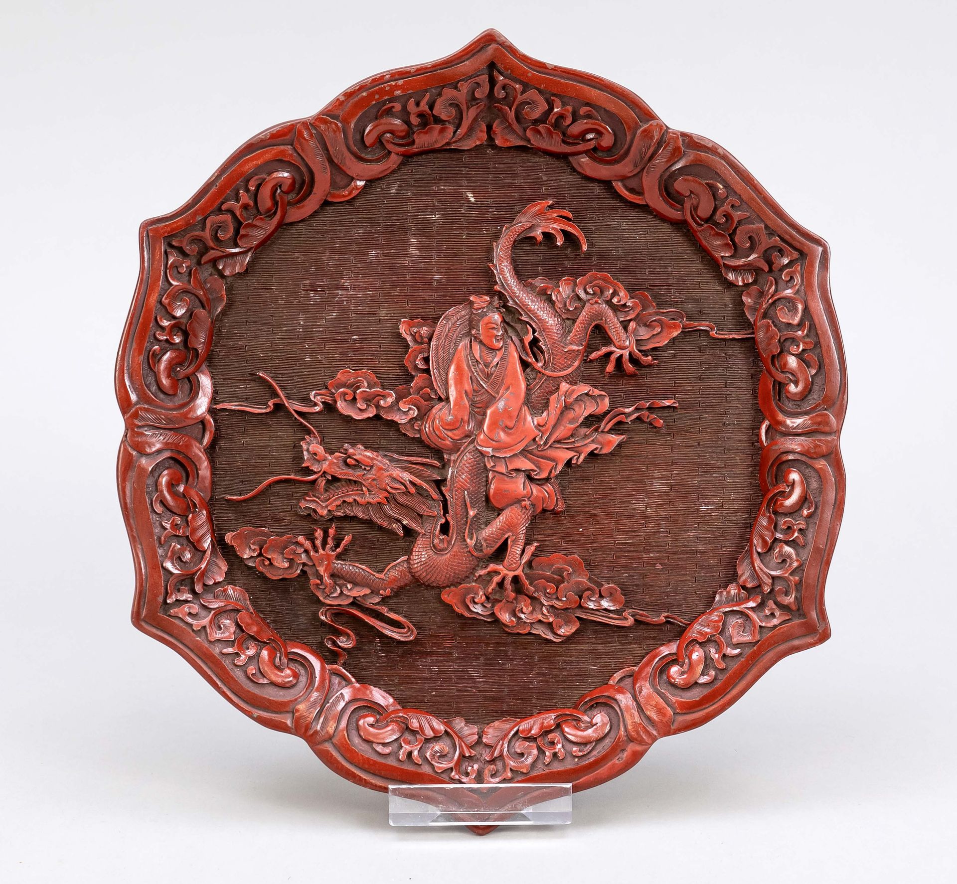 Null 伪朱砂雕漆，中国，20世纪，有叶的形式为莲花。镜中的观音骑在一条蠕动的龙上，在风格化的云带之间，长24厘米。