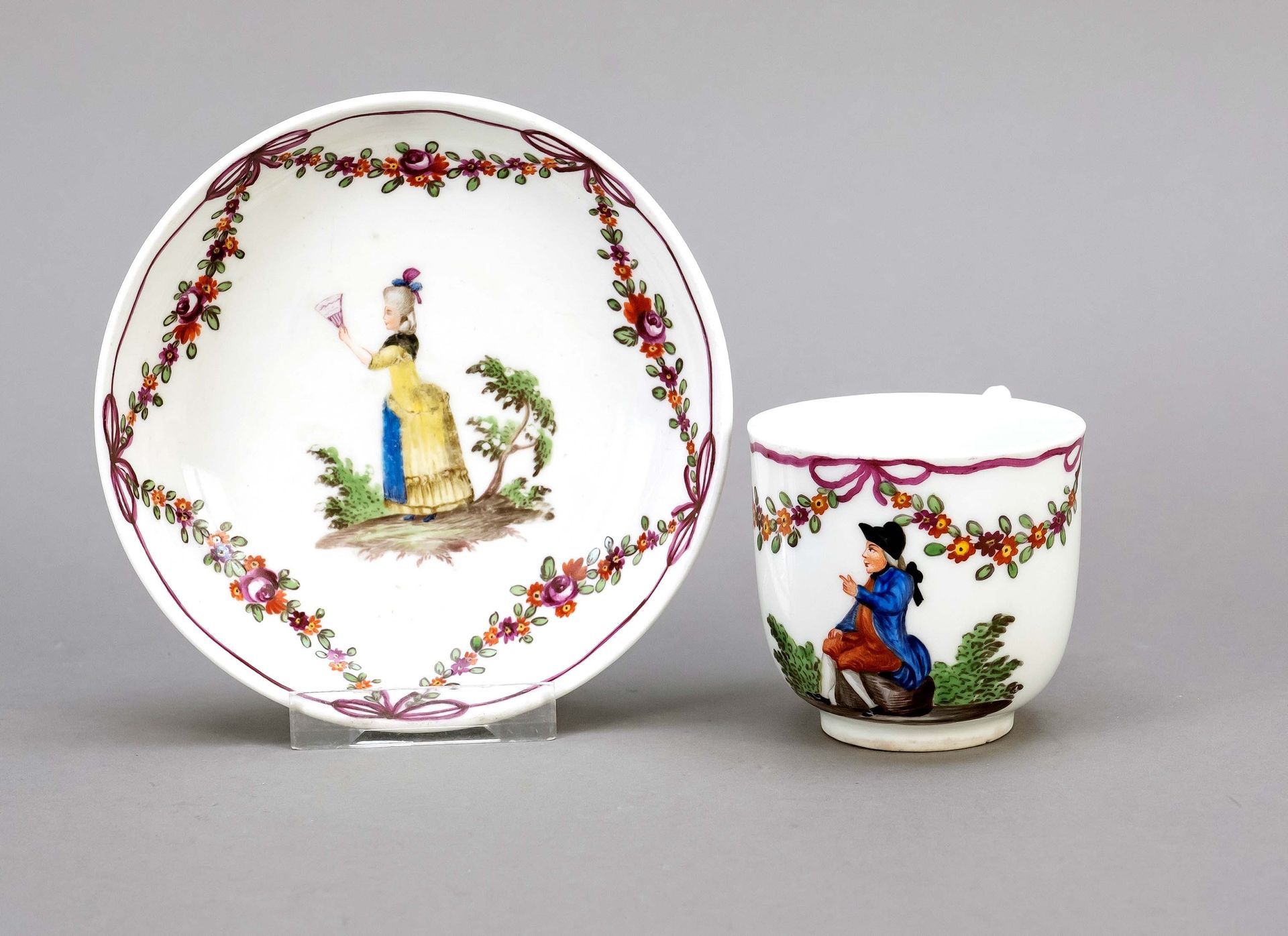 Null 带UT的杯子，维也纳，19世纪，杯子有尖折的把手，多色画，杯子上有一个戴着两角帽的人，碟子上有一个拿着扇子的女士在风景中，周围有花环，高7,5厘米