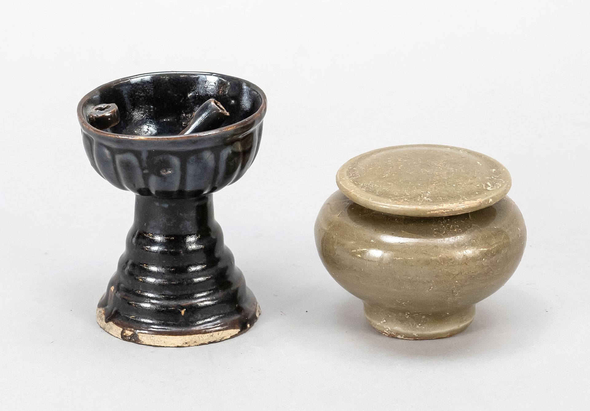 Null 2件单色釉瓷器，中国，宋代。灰绿釉小盖罐(高5/D. 7厘米)和高底座上有裂纹的油灯，釉面为棕黑色(高7.5厘米)。