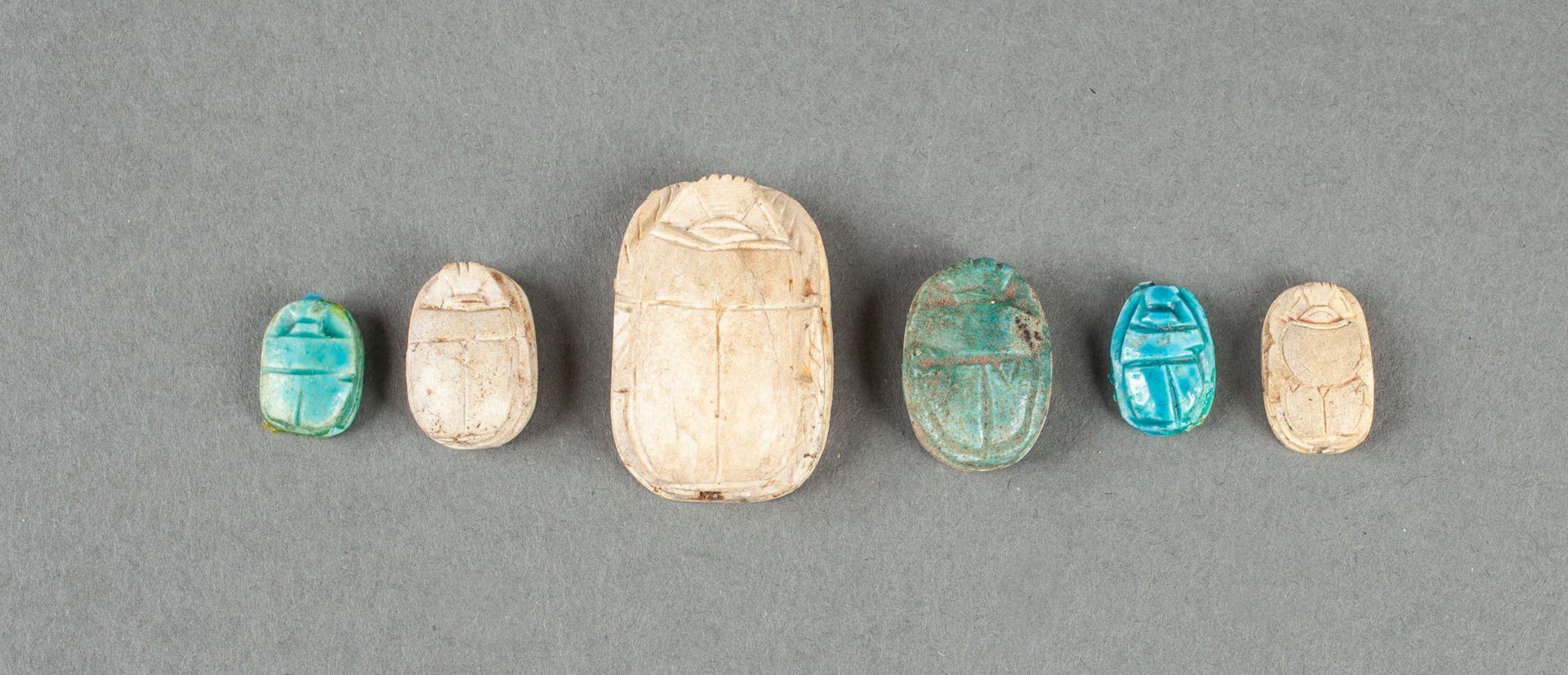Null Un set di sei scarabei iscritti in terracotta blu in stile egiziano.

Da 1,&hellip;