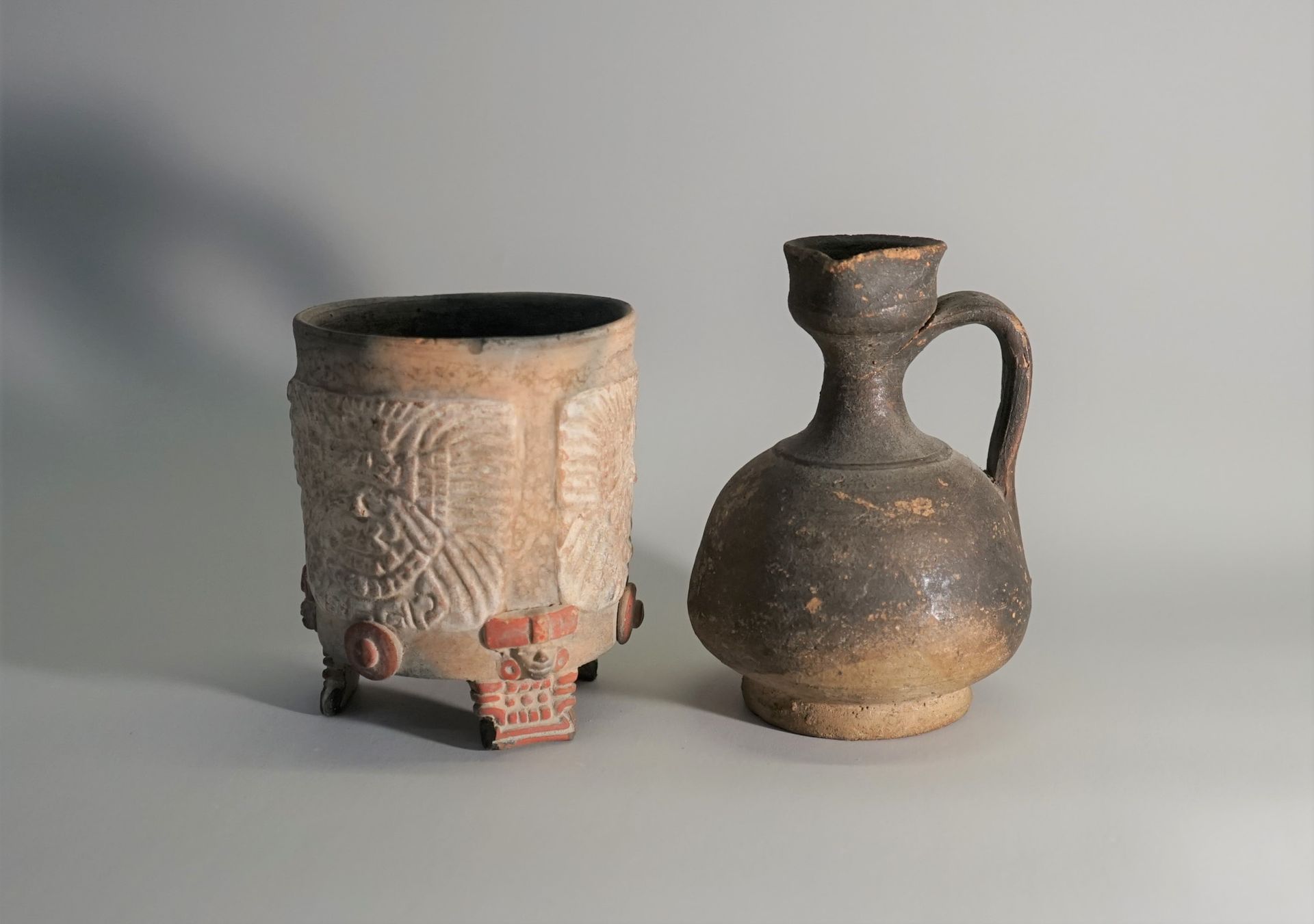 Null 一套两个赤土容器，一个是玛雅风格的，三脚站立，装饰有面具。另一个是有米色和棕色手柄的小壶。

11.5厘米和10厘米